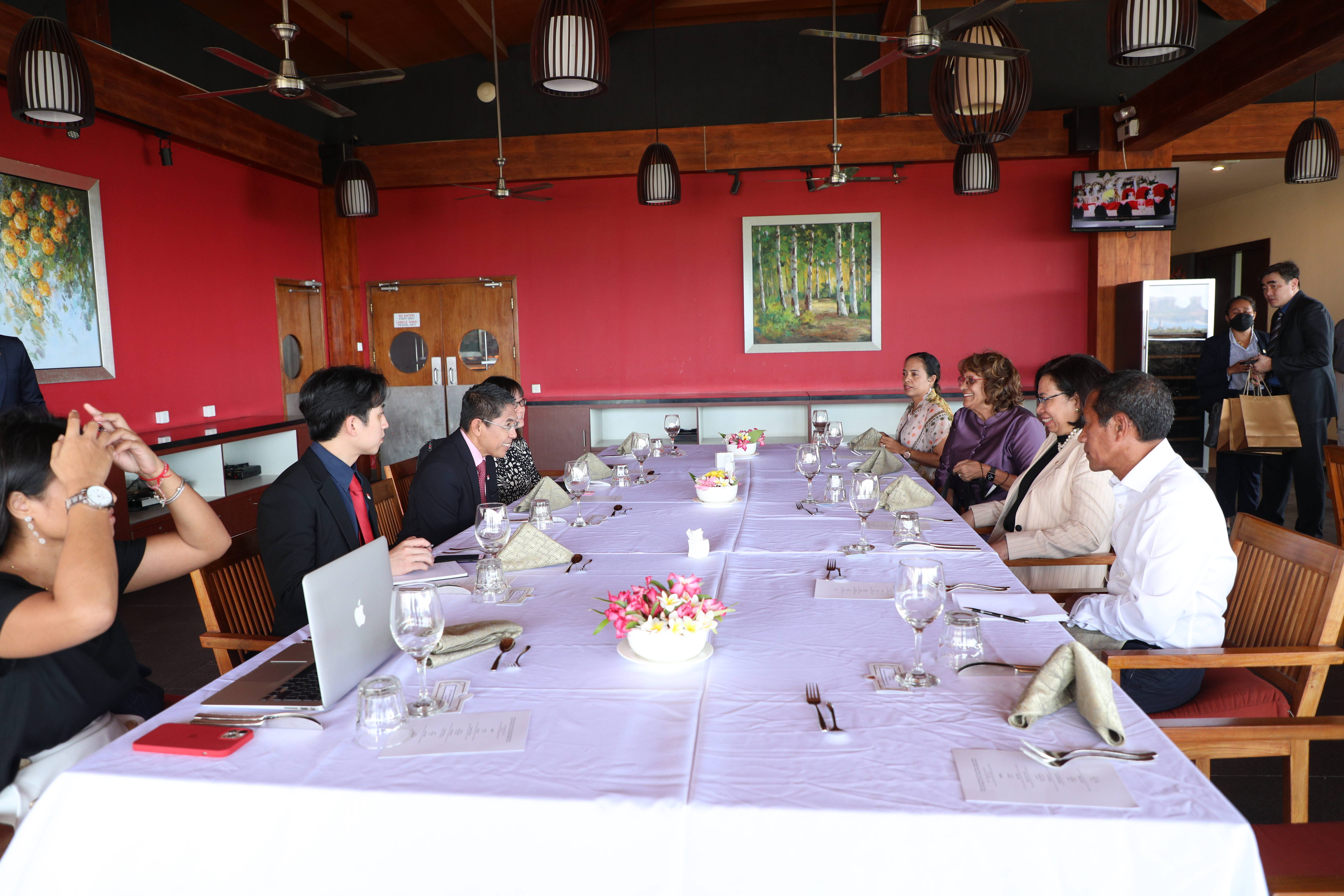 People seated at a long, set table inside a room with red walls and ceiling fans.