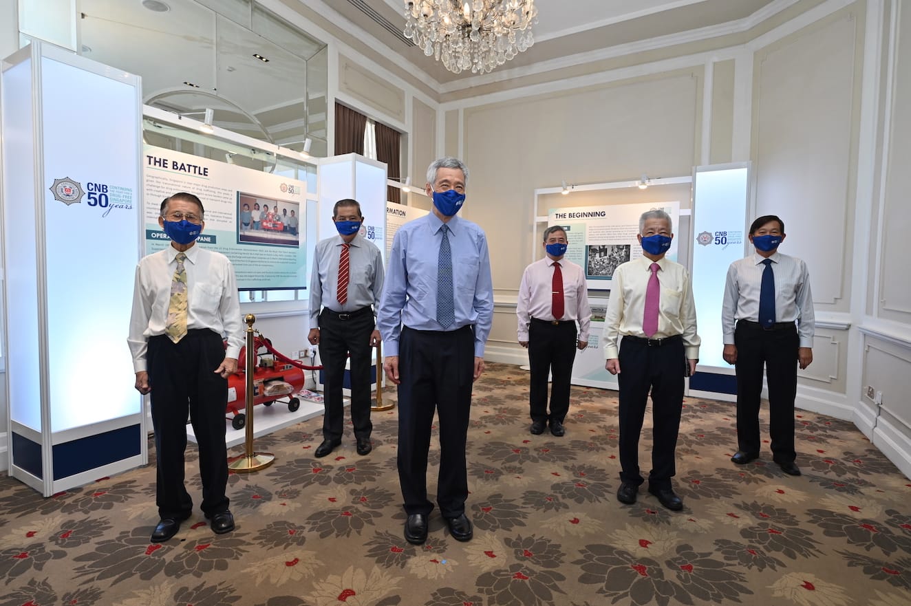 Six men in suits and blue masks stand in front of CNB 50th anniversary displays.