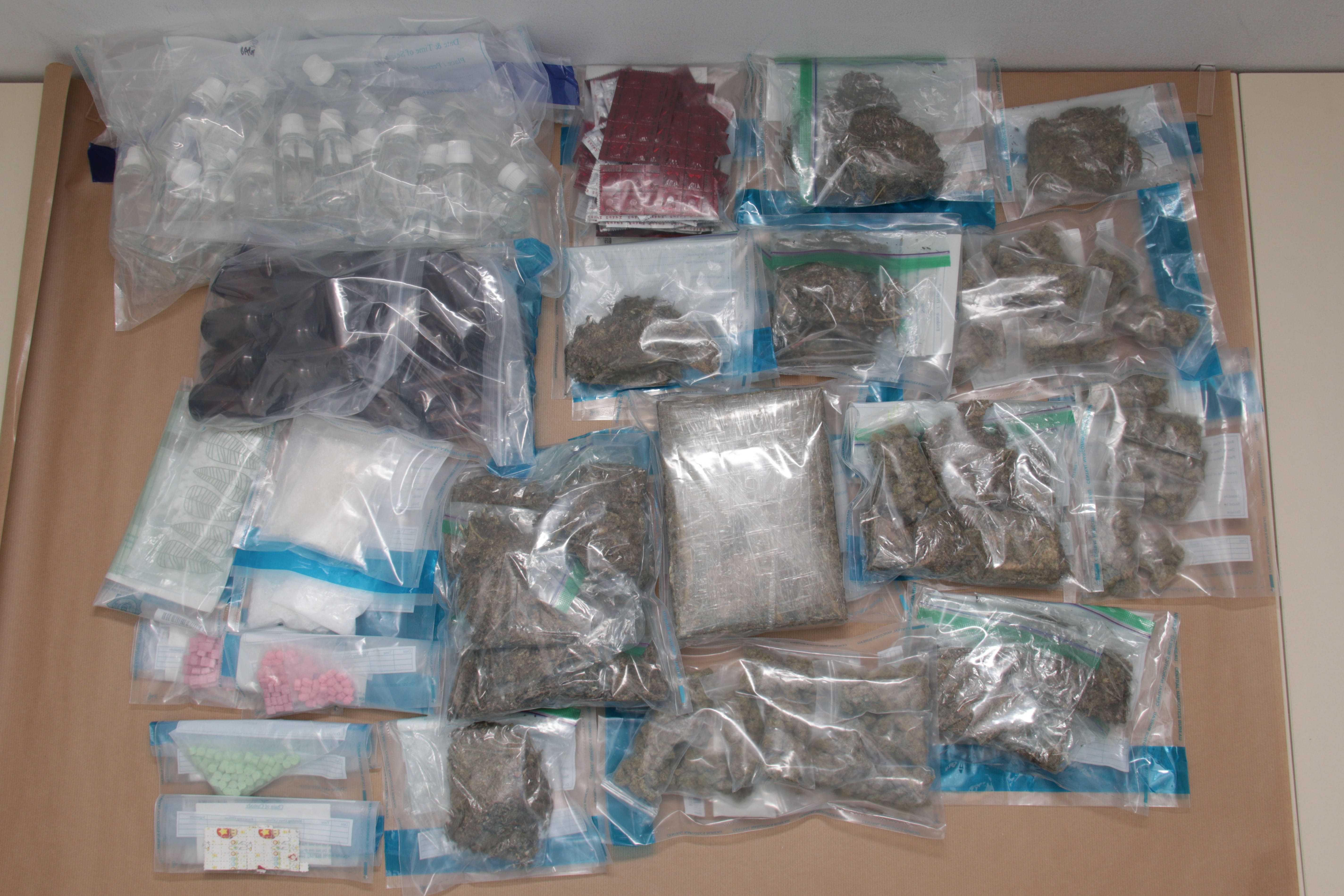 Multiple clear bags of various substances: pills, powder, liquids, marijuana on a brown surface.