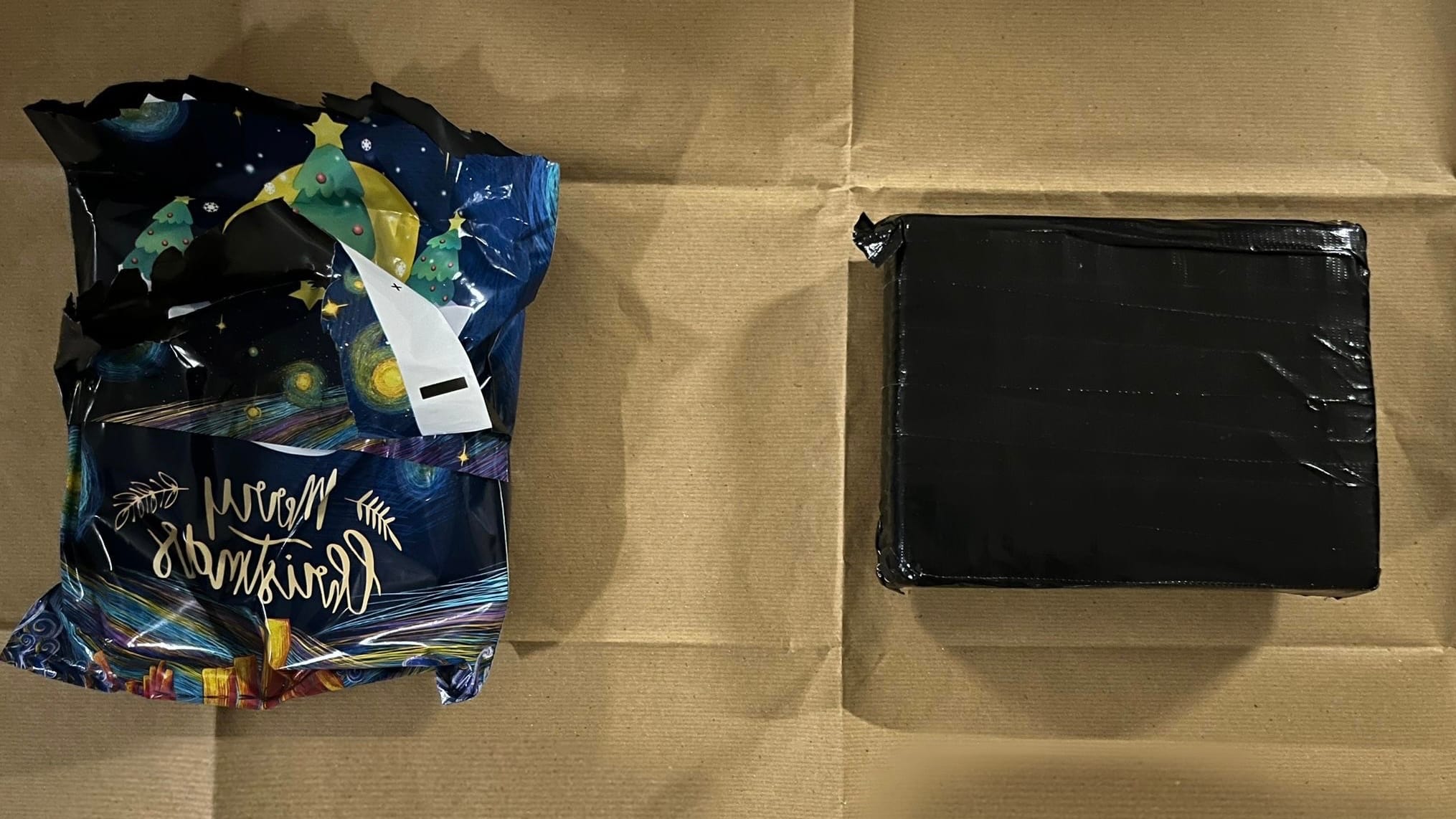 Wrapped Christmas gift beside black duct-taped square object on a brown surface.