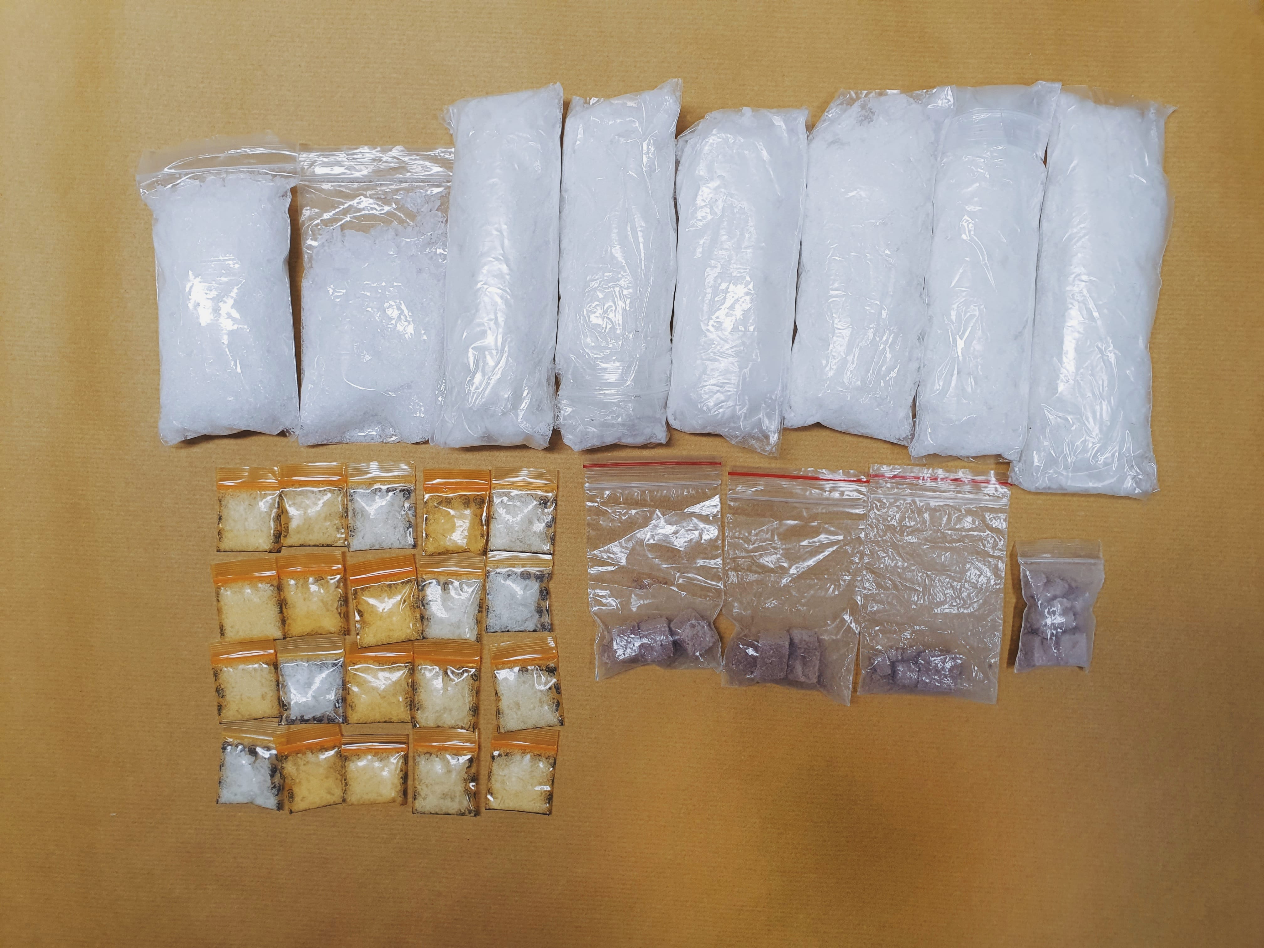 Plastic bags of white crystal-like substances, smaller bags with brown and purple pills on a tan surface.