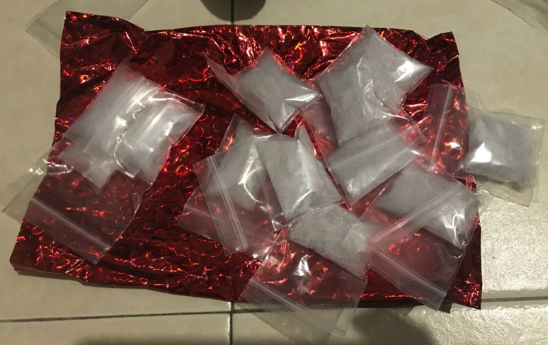 Small plastic bags containing white granules on red shiny material.