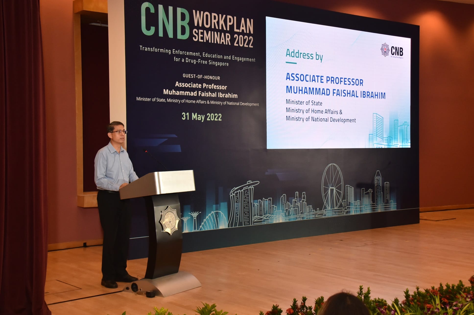 Man at podium, CNB Workplan Seminar 2022 backdrop with Singapore skyline.