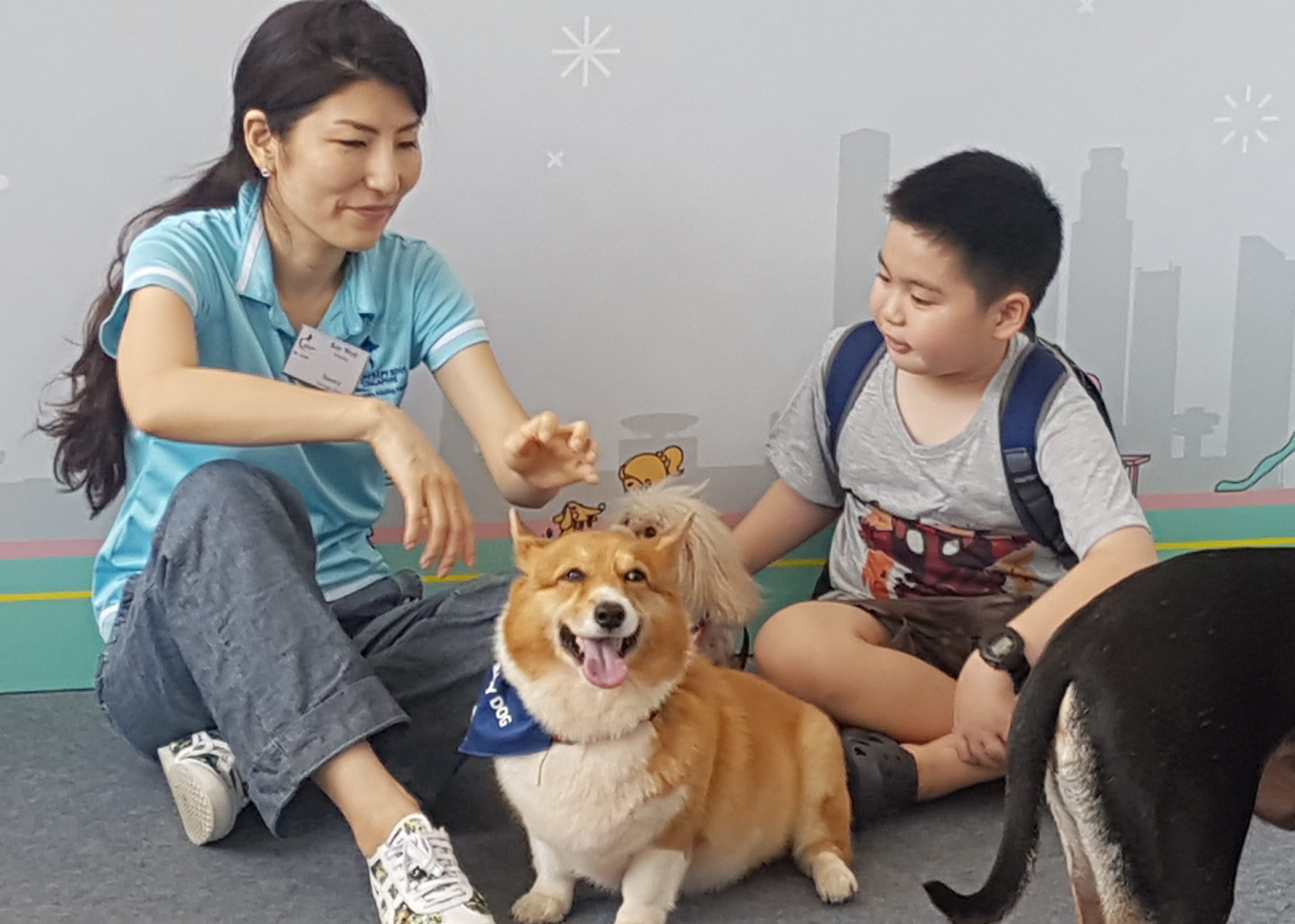Woman, boy, and three dogs sitting near a city skyline wall graphic.