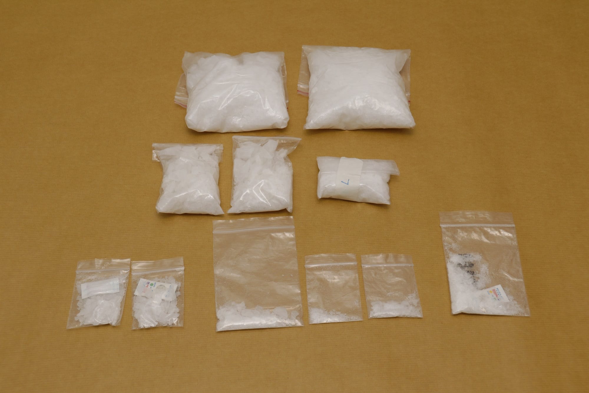 Multiple clear plastic bags with white crystalline contents on a tan surface.