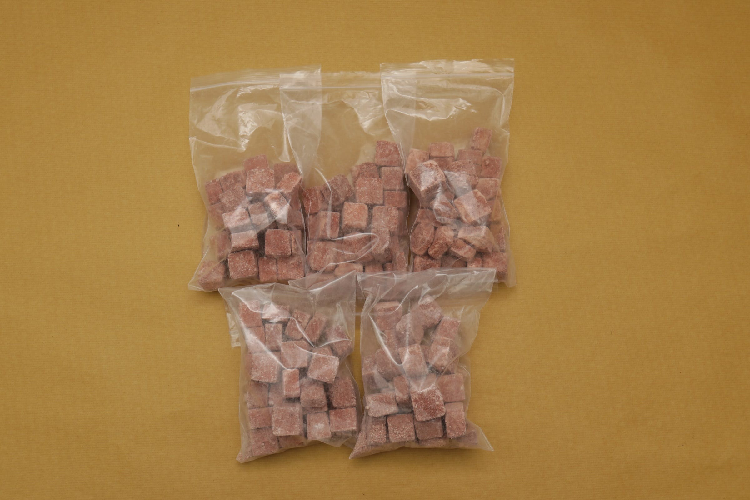 Four clear plastic bags filled with reddish-brown frozen cubes on a yellow surface.