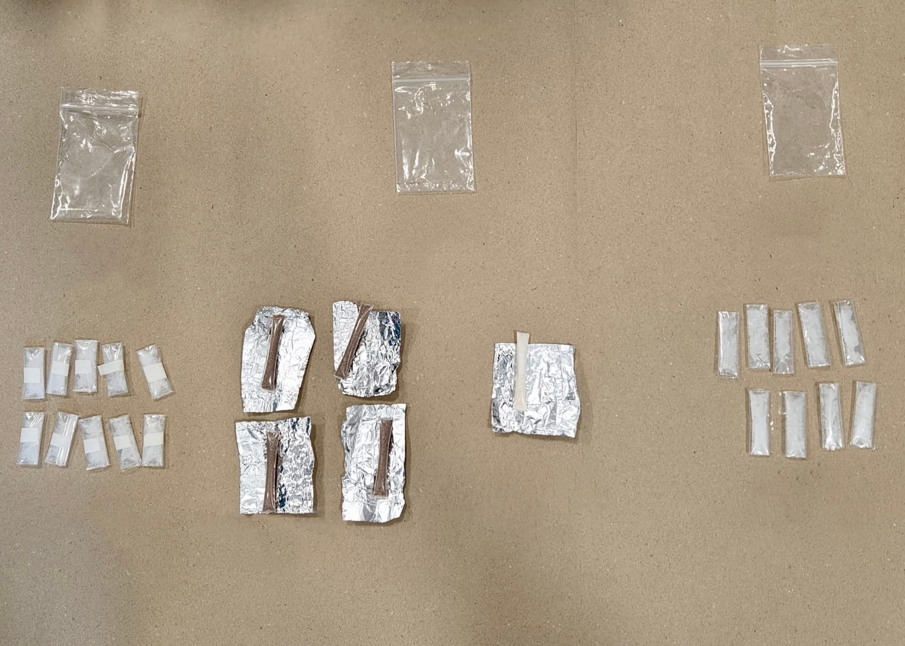 Clear plastic bags, some empty, some with white contents, and foil packets with brown contents on a tan surface.