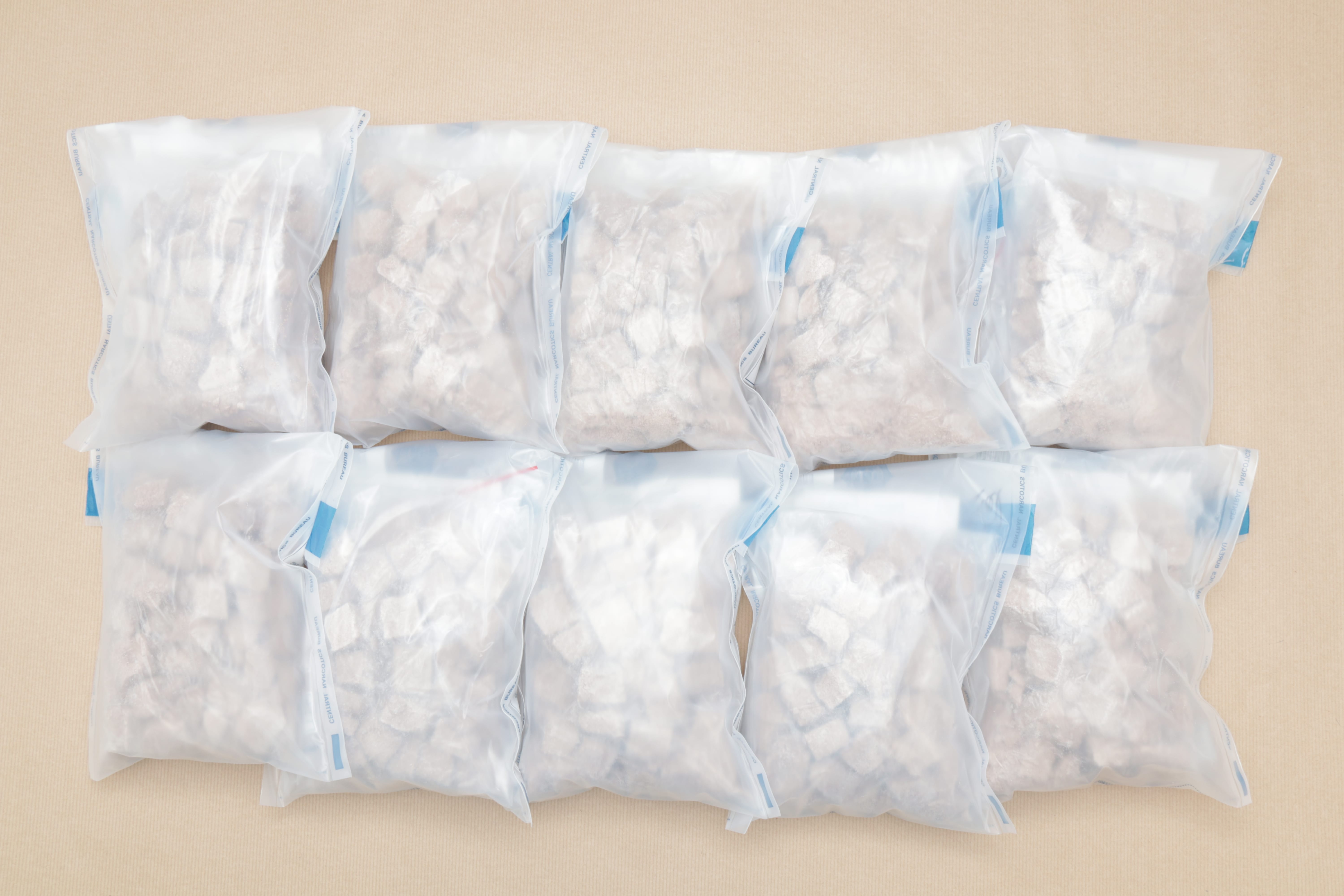 Ten clear plastic bags filled with irregular white chunks on a light brown surface.