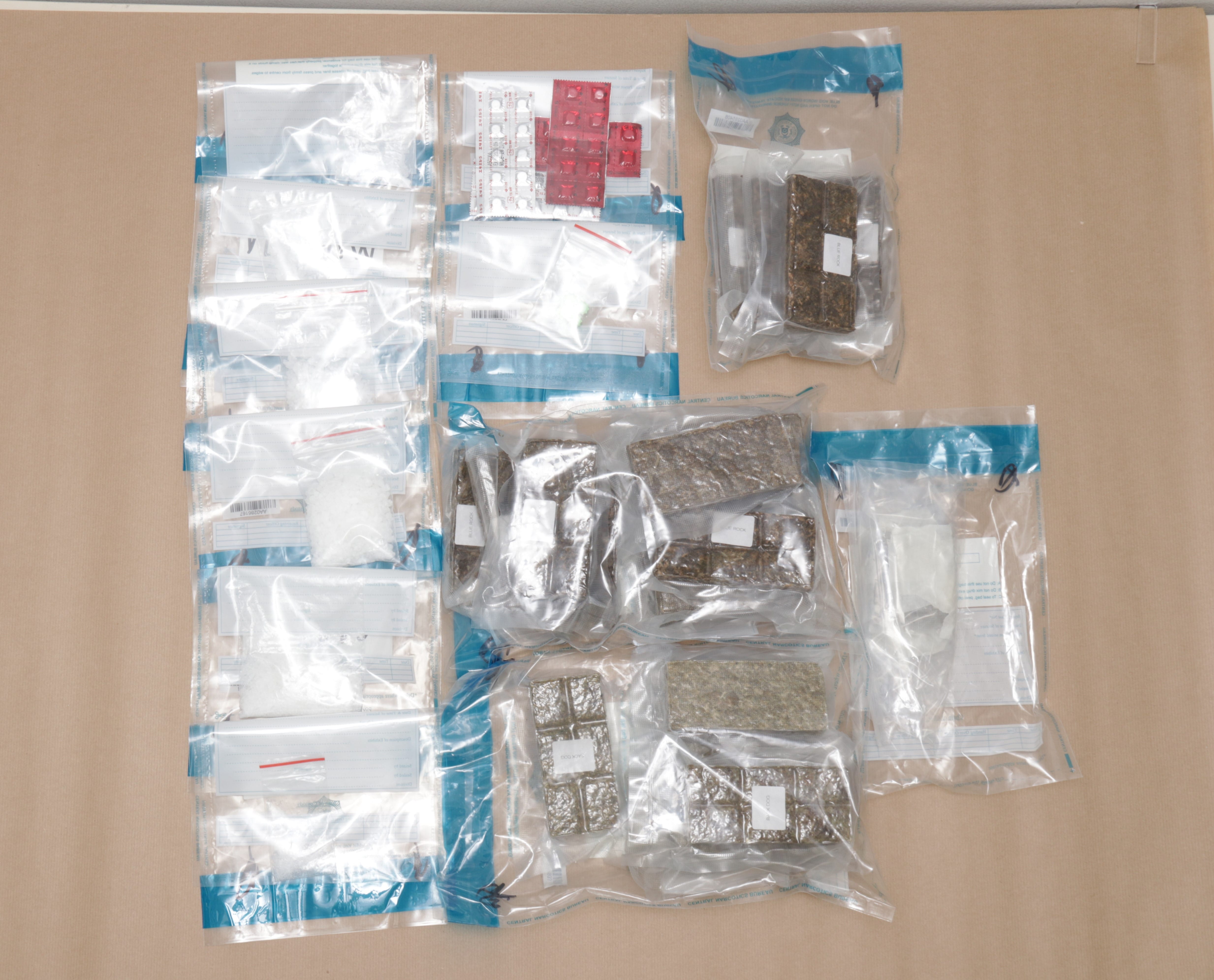 Sealed evidence bags containing pills, white powder, and brick-shaped hashish on a table.