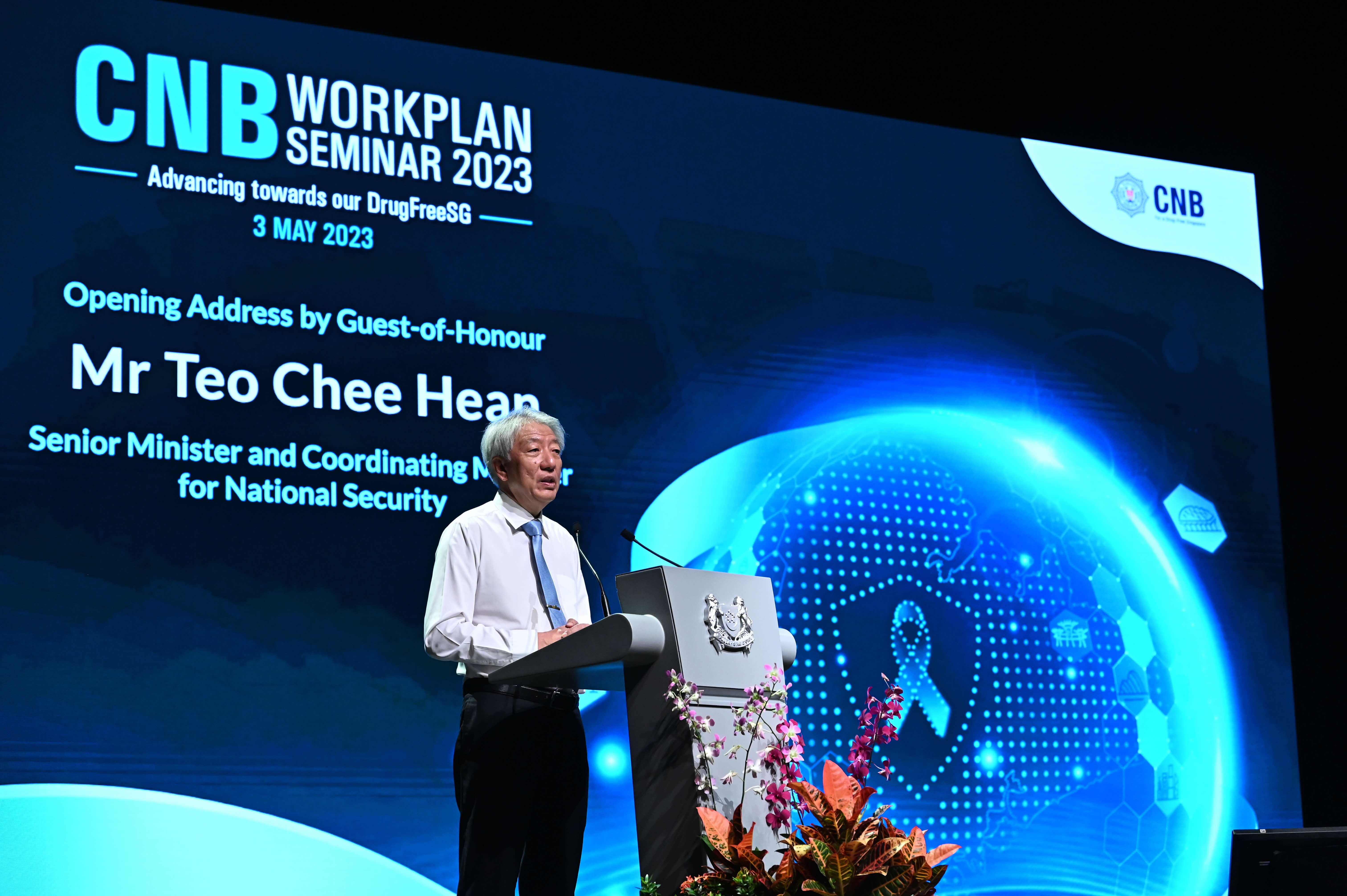 Man at CNB Workplan Seminar lectern with blue digital backdrop.