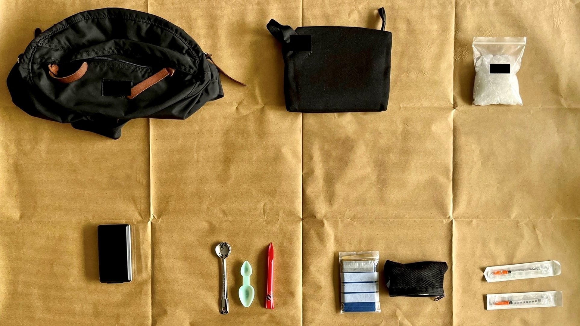 Items: backpack, pouches, phone, spoons, syringes, and bag with white crystals, on brown paper.