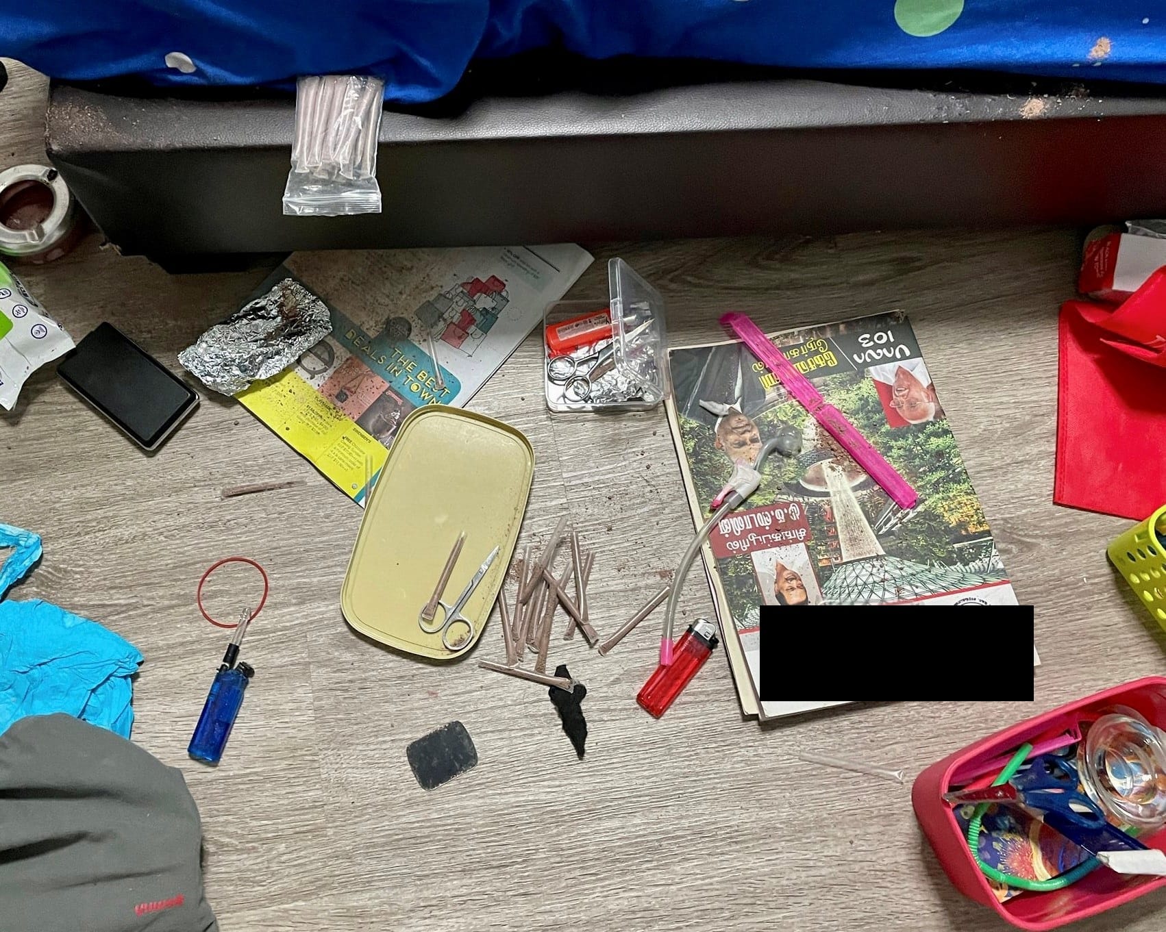 Floor with drug paraphernalia including lighters, pipes, tray, foil, and magazines.
