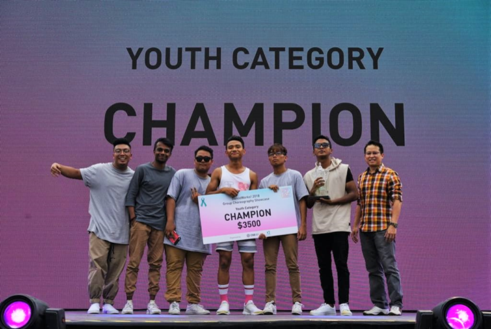 Seven young men on stage hold a prize check labeled "CHAMPION $3500". Text on screen reads "YOUTH CATEGORY CHAMPION".