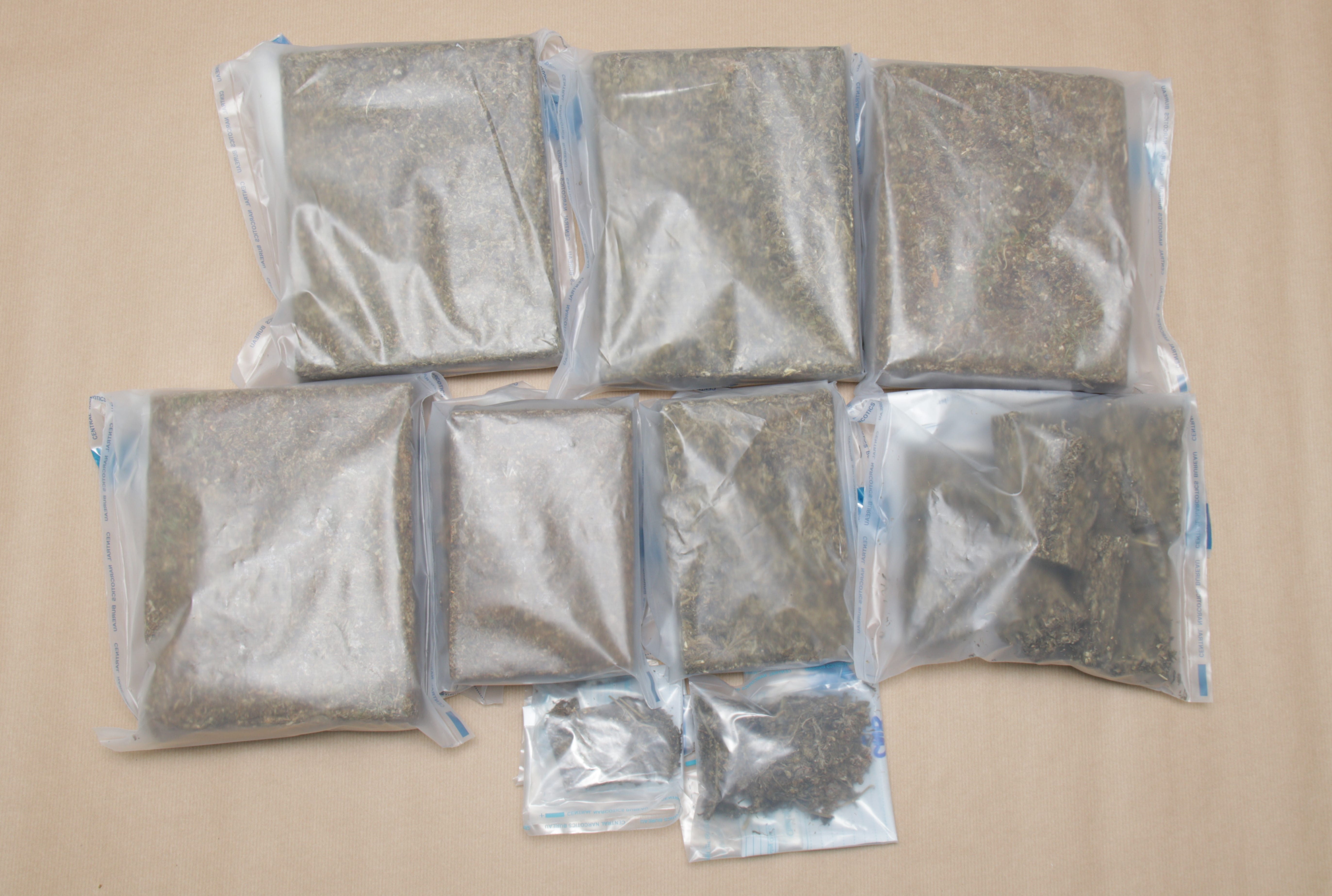 Nine clear plastic bags filled with dried herbs arranged on a tan surface.