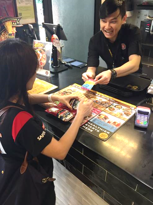 Customer at counter passing card to a cashier in a black shirt with a logo.