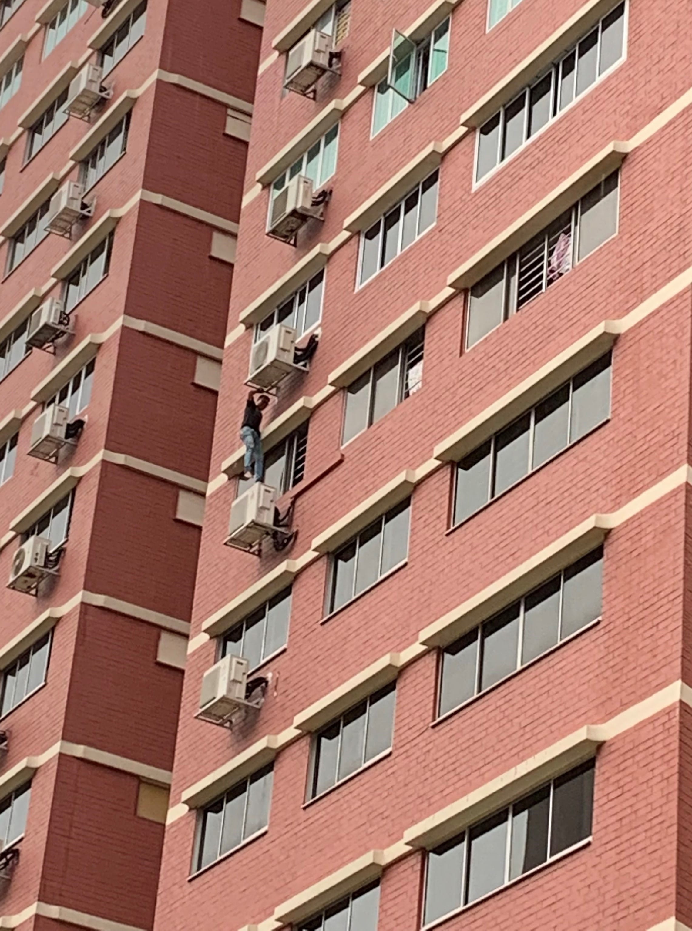 Brick building exterior showing a person climbing on window air conditioning units.
