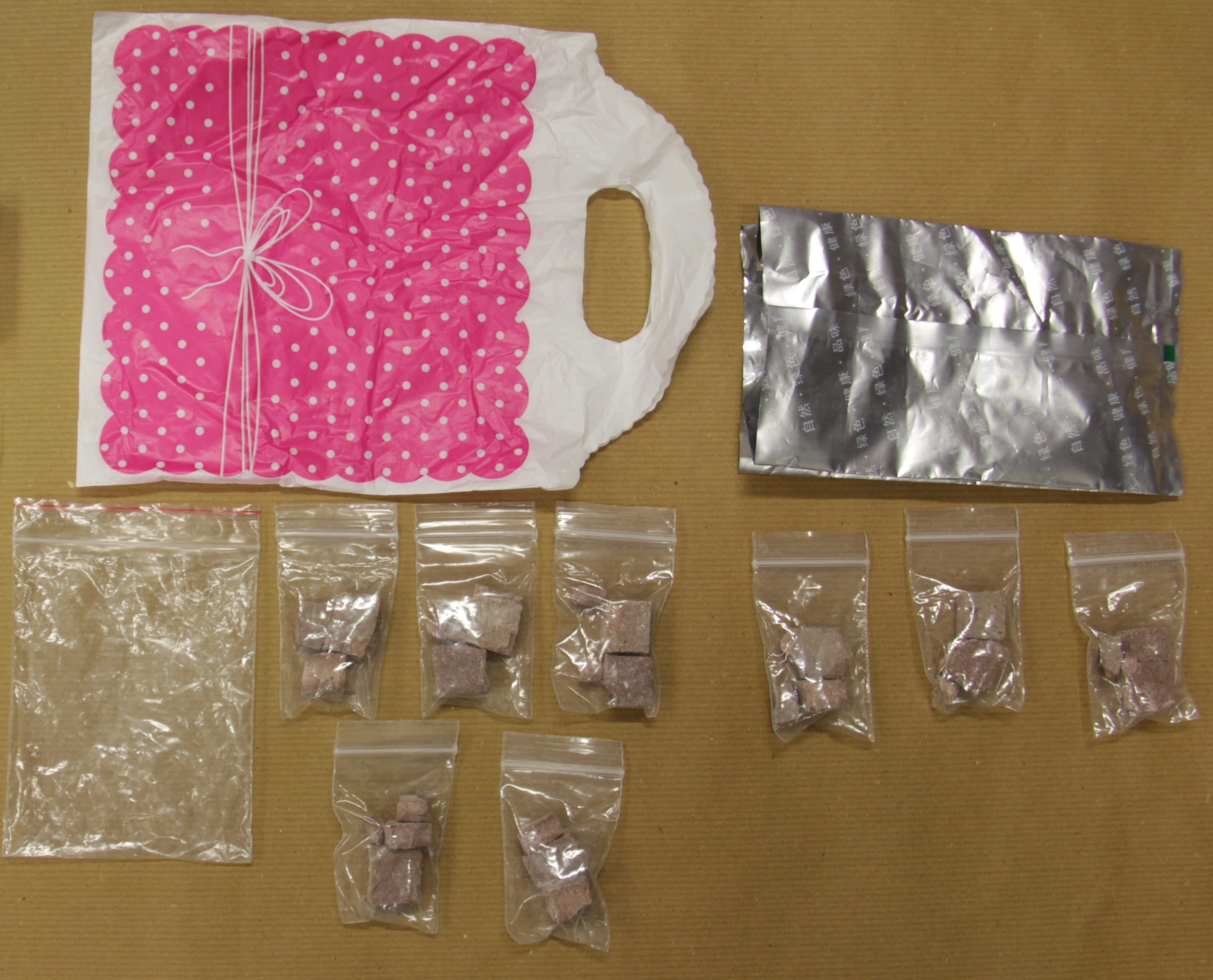 Pink polka-dot bag, foil packet, & baggies filled with pink cubes on a brown surface.