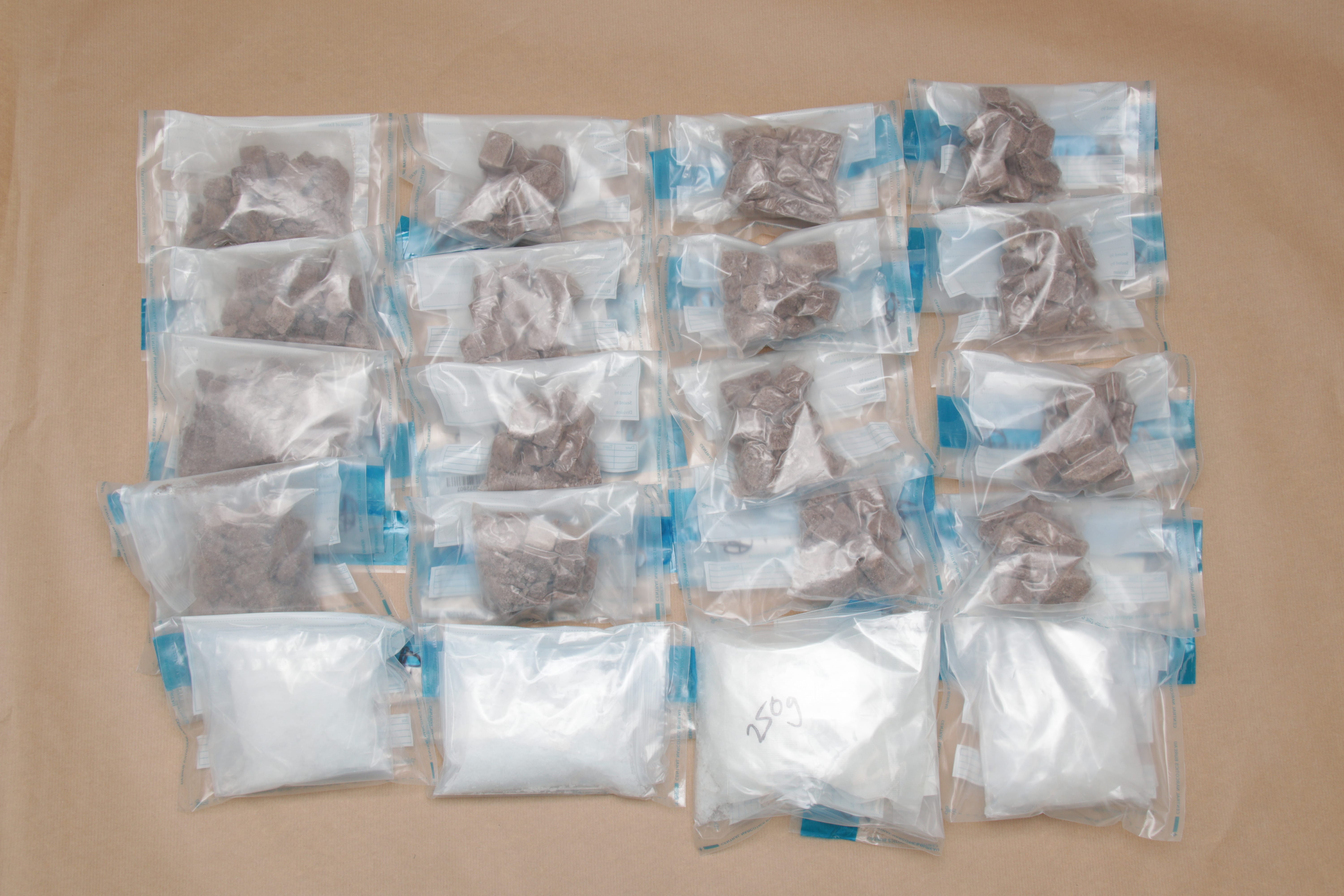 Arrangement of sealed plastic bags, some with brown chunks, some with white powder, on a brown surface.