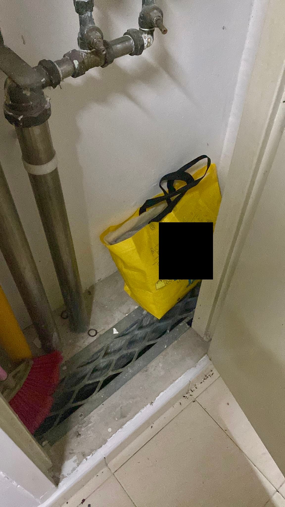Pipes and a yellow bag with a black square obscuring part of it, resting on a metal grate.