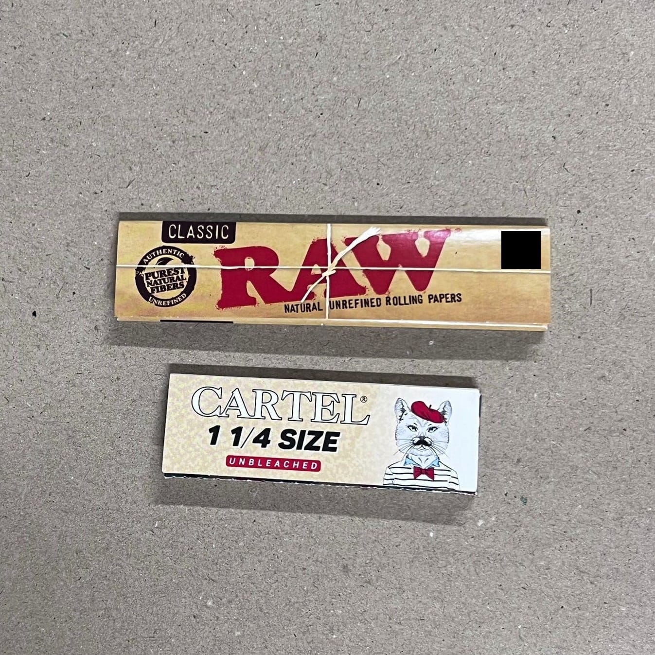 Two packs rolling papers: RAW classic, and Cartel 1 1/4 with cat illustration.