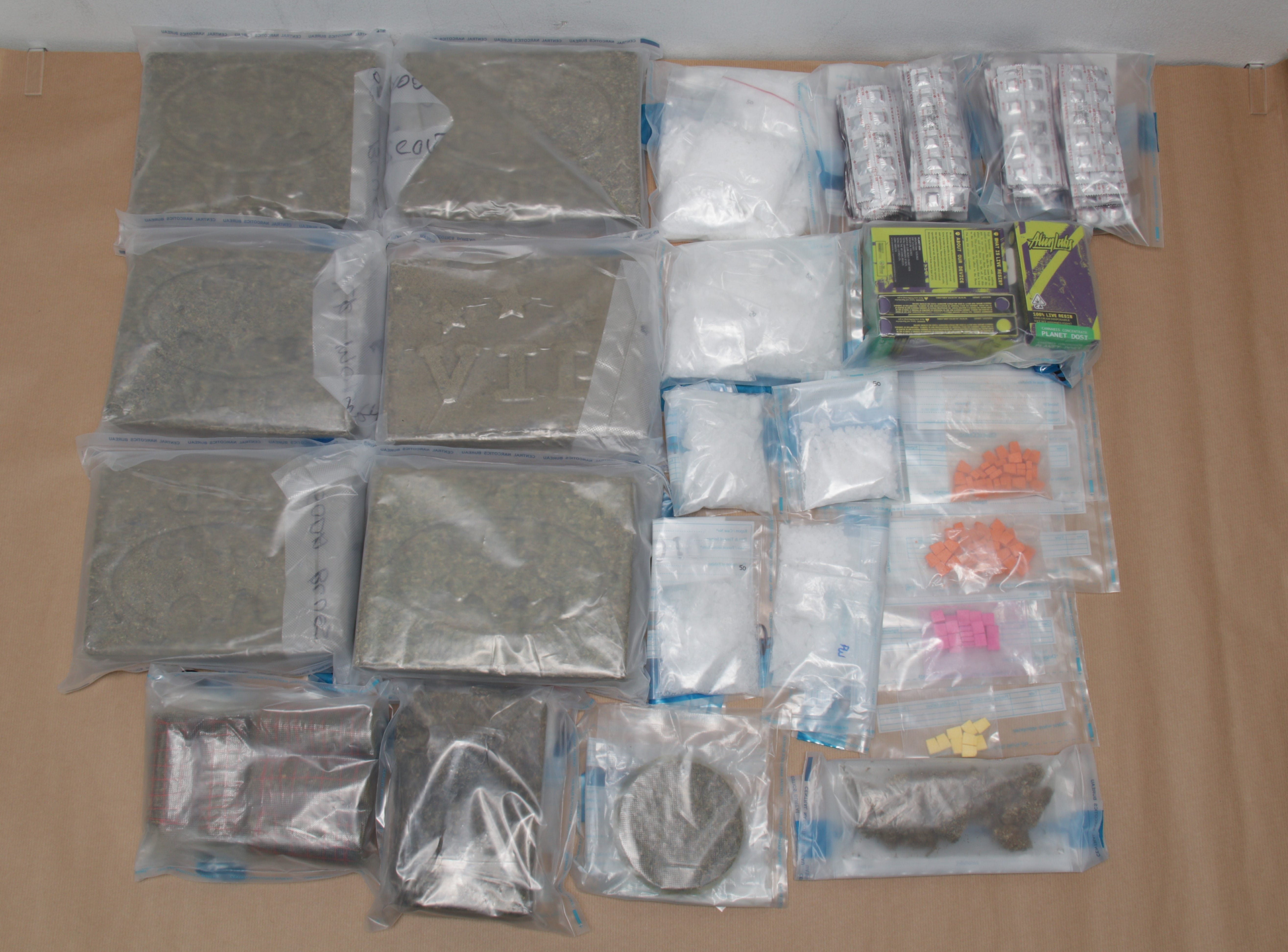 Bags of marijuana, white powder, pills, and Alien Labs cannabis product on a brown surface.