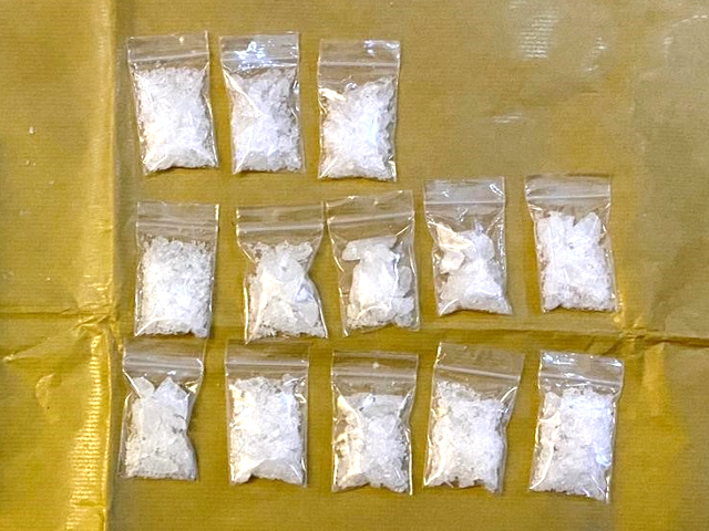 Eleven small, clear bags with white crystalline contents arranged on a tan surface.