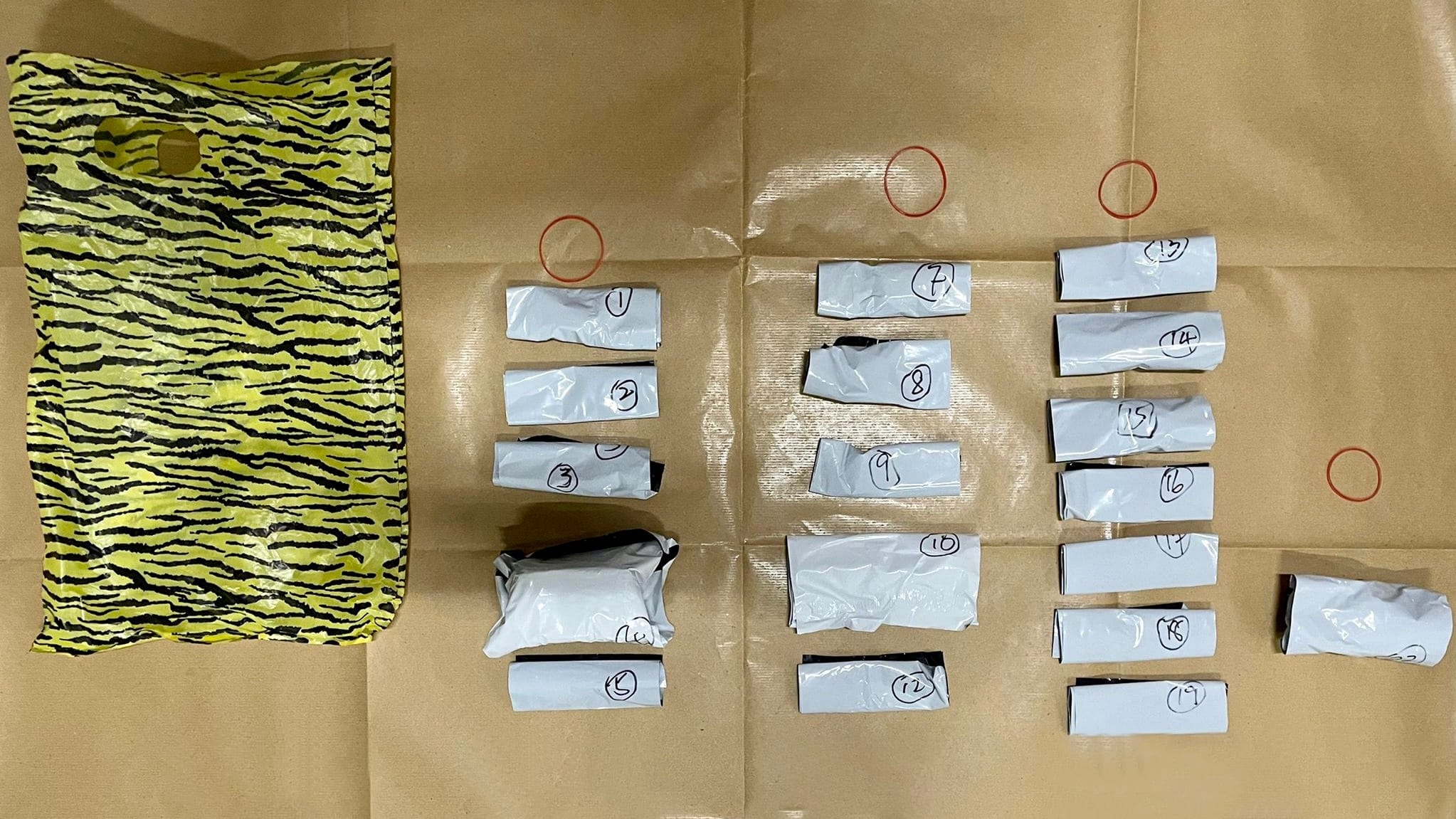 Yellow tiger-striped plastic bag and 12 small white numbered packages on a brown surface with rubber bands.