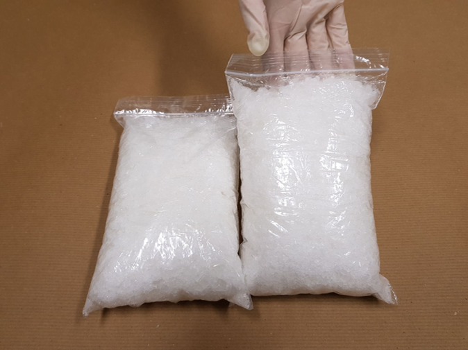 Two clear bags filled with white crystal-like substance; gloved hand near one bag.