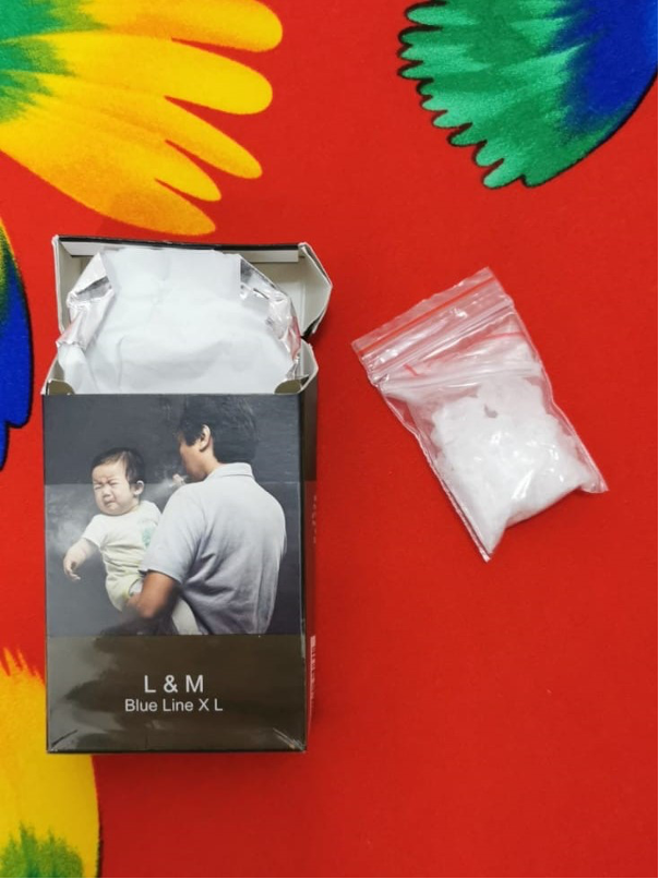 Open L&M cigarette pack with a bag of white crystals on a red floral surface.