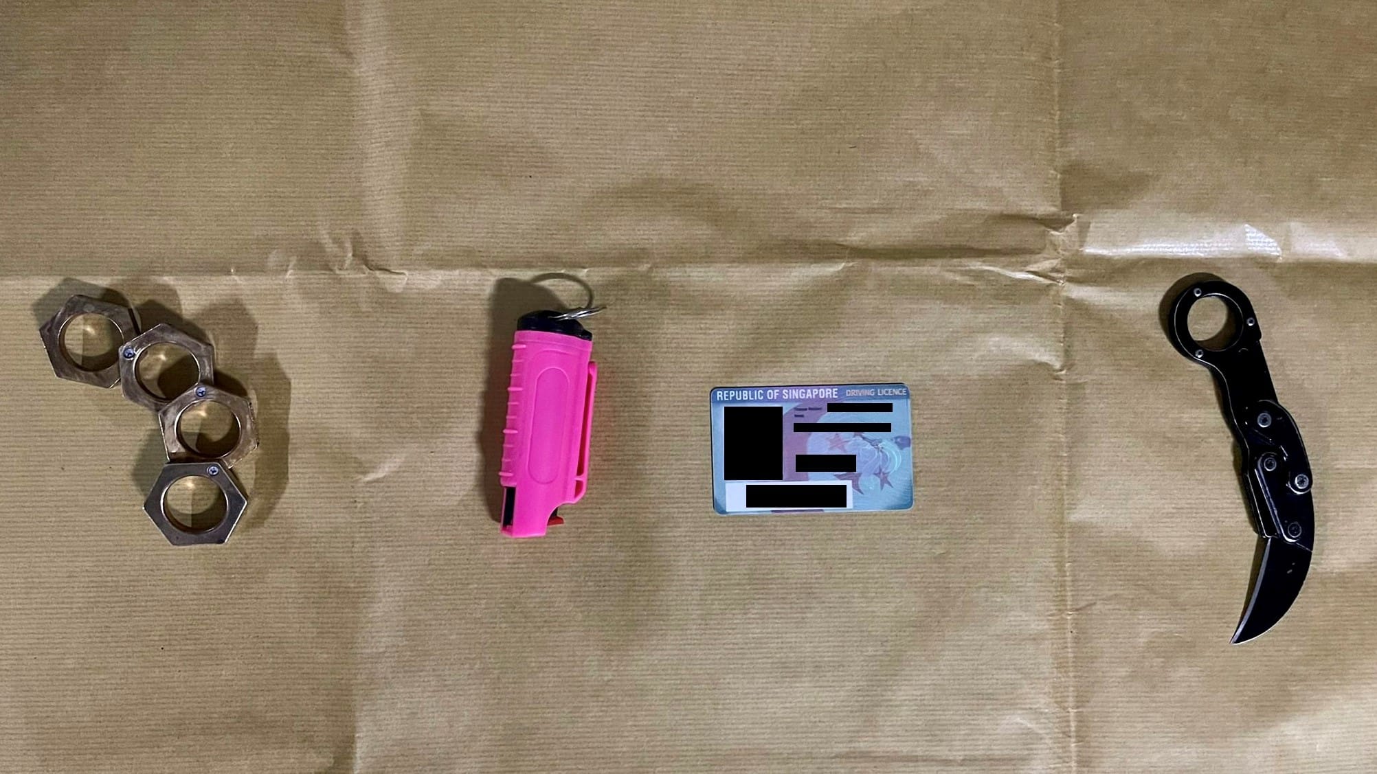 Brass knuckles, pink stun gun, Republic of Singapore driver's license, and karambit knife on tan paper.