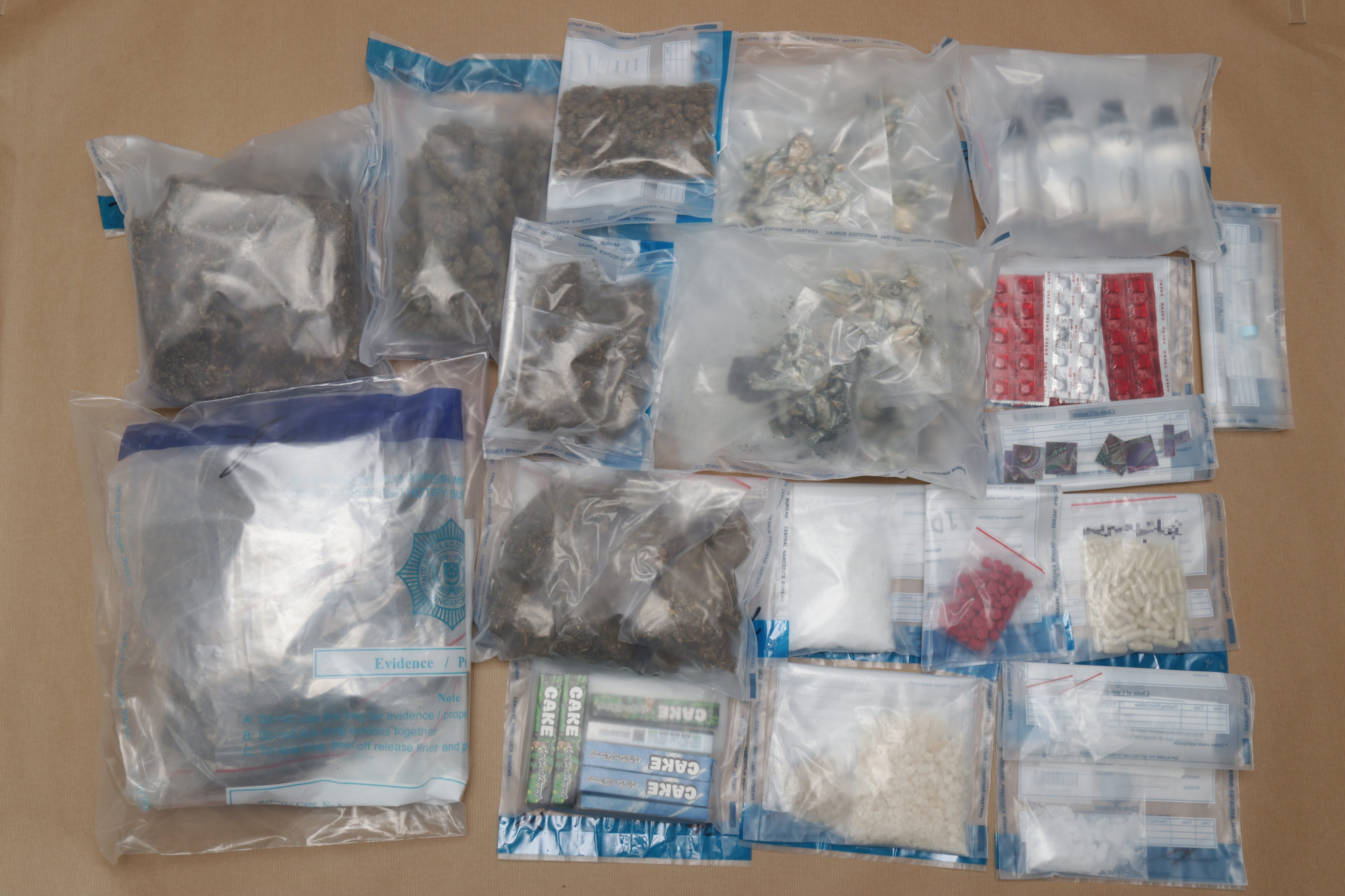 Multiple evidence bags containing various suspected drugs and paraphernalia on a brown surface.