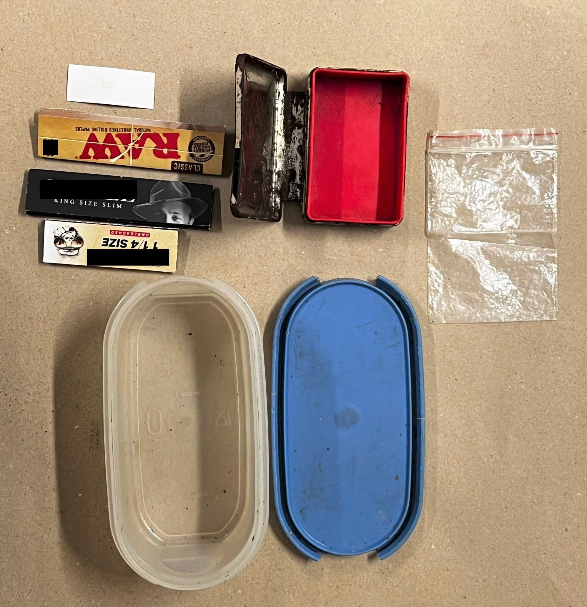 Rolling papers (RAW, King Size), metal/plastic containers, and small resealable bags on a tan surface.
