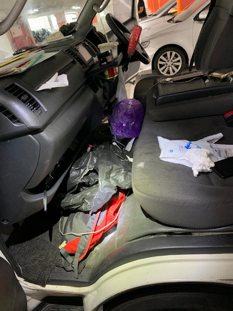 Cluttered passenger side of a white van; trash bags and belongings fill footwell and seat.