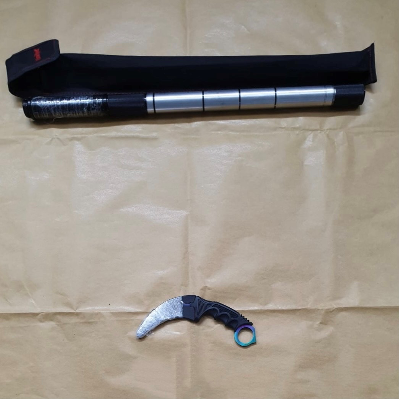 Telescopic baton with a sheath and a curved karambit knife, on brown wrinkled paper.