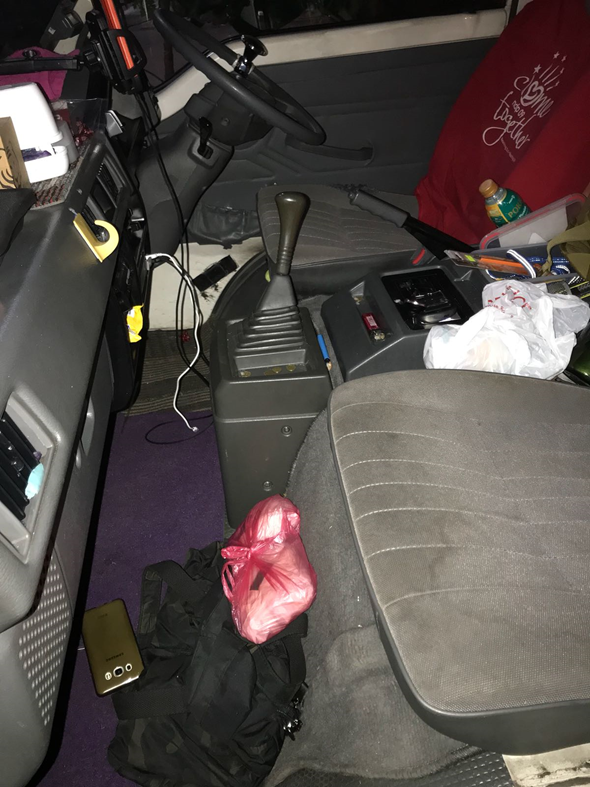 Truck cab interior with gear stick, cluttered with items on seat and floor.