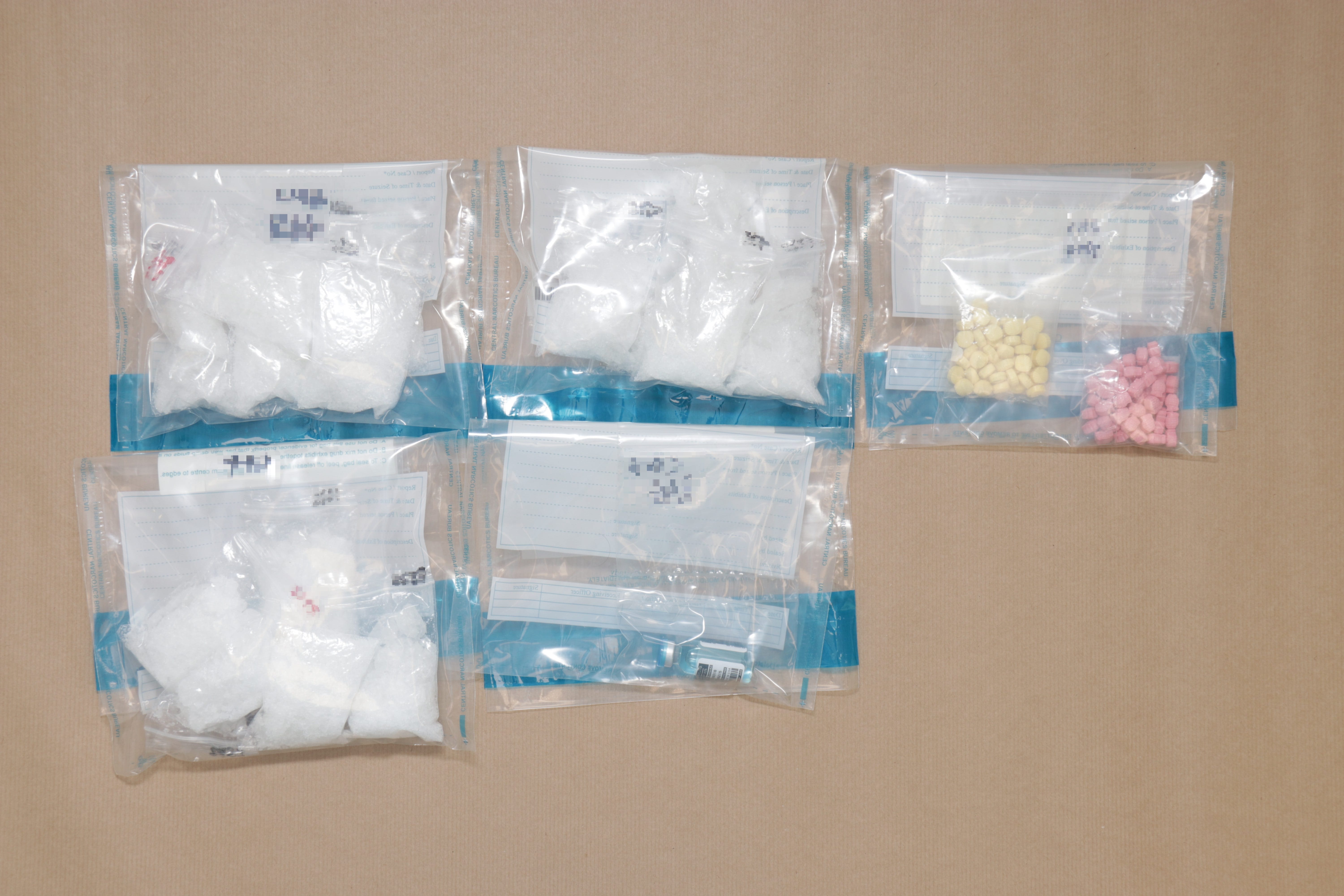 Five plastic bags: four with white powder, one with yellow and pink pills, on brown surface.