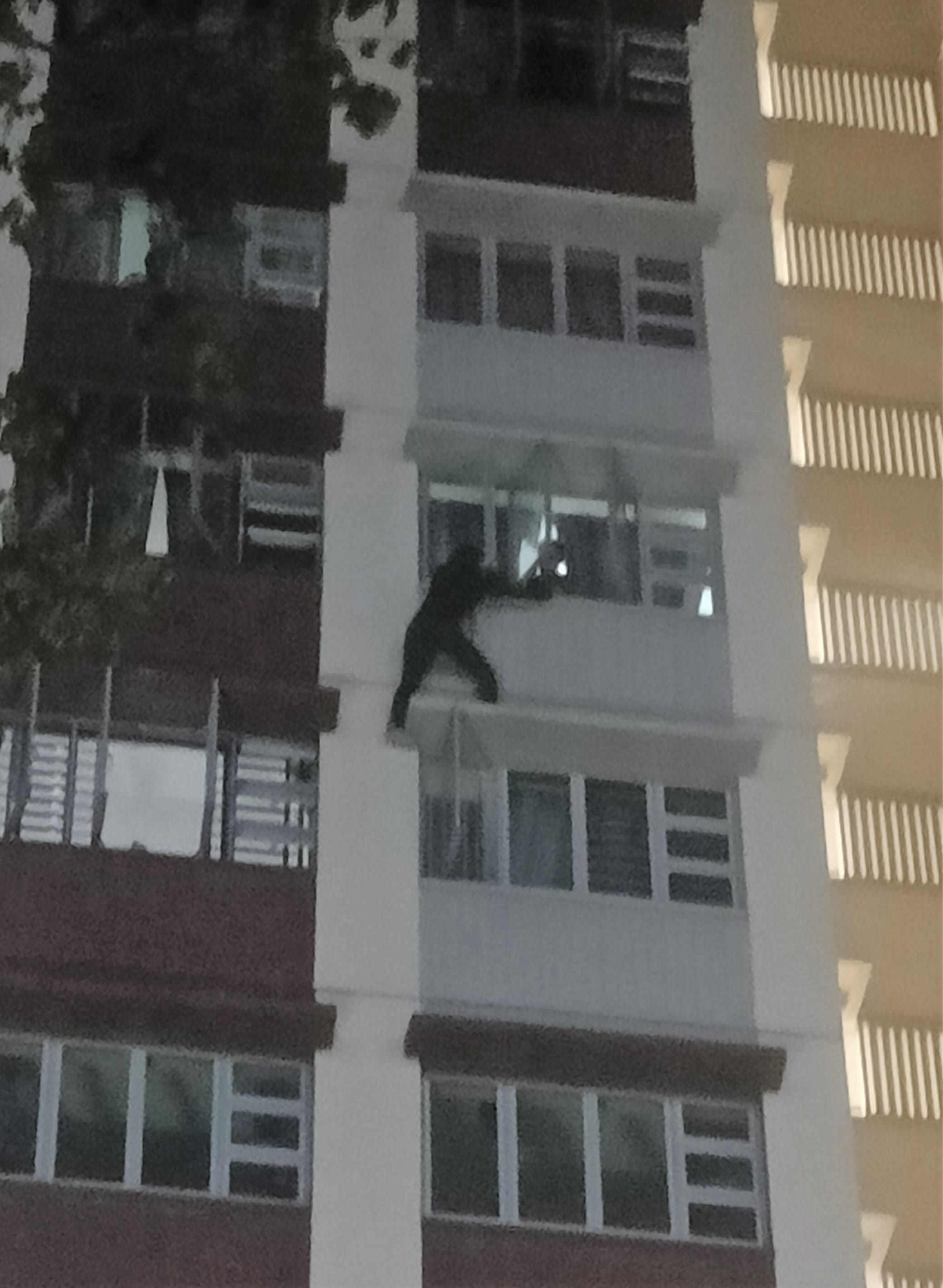 Person in dark clothing climbs outside of a building between windows.