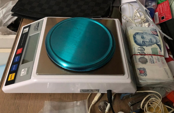Digital scale with blue platform next to bundled Singapore dollar bills.