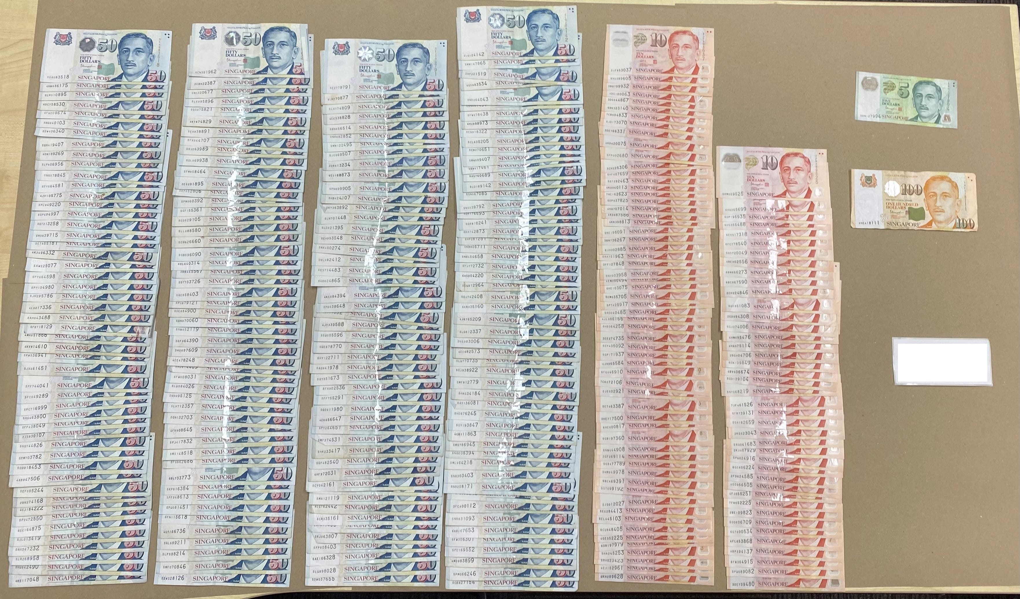 Stacks of Singapore dollar banknotes; mostly 50s, some 10s, 5s, and 100s.