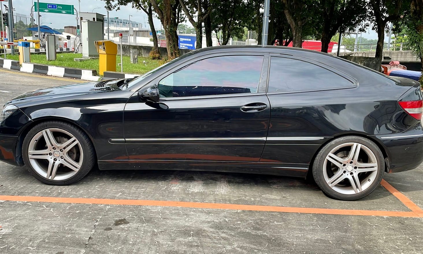 Black Mercedes-Benz coupe parked on gray asphalt with orange lines.