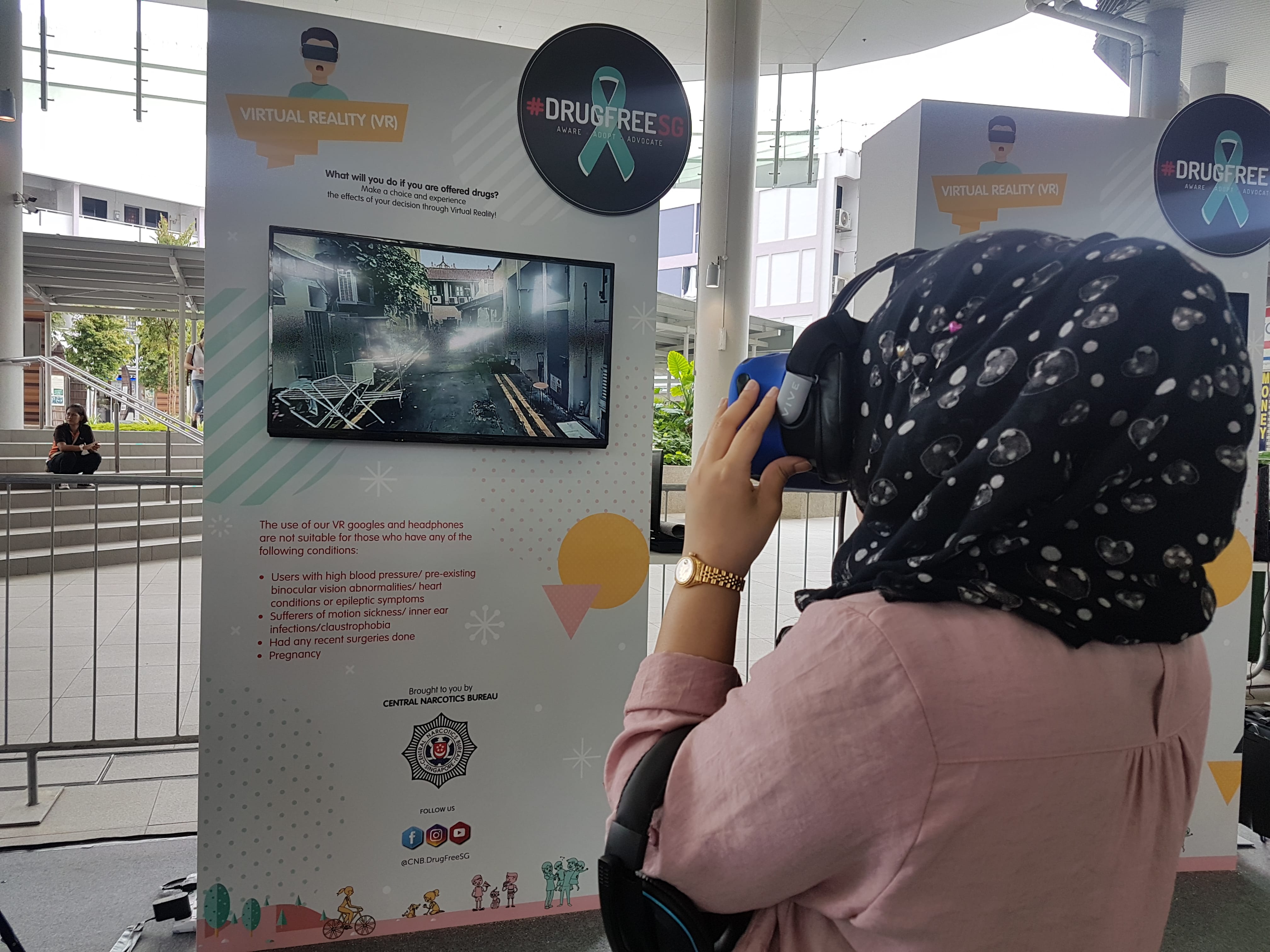 Person wearing a VR headset at a #DrugFreeSG booth with virtual reality display.