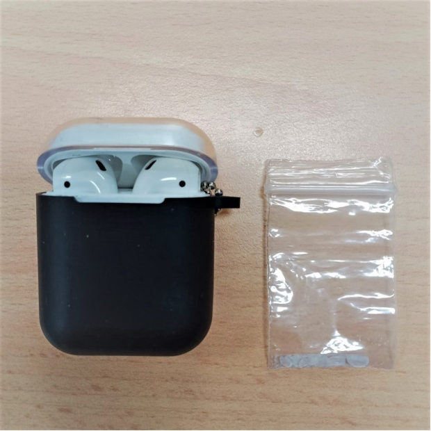Open AirPods case with earbuds and a small plastic bag on a wood surface.