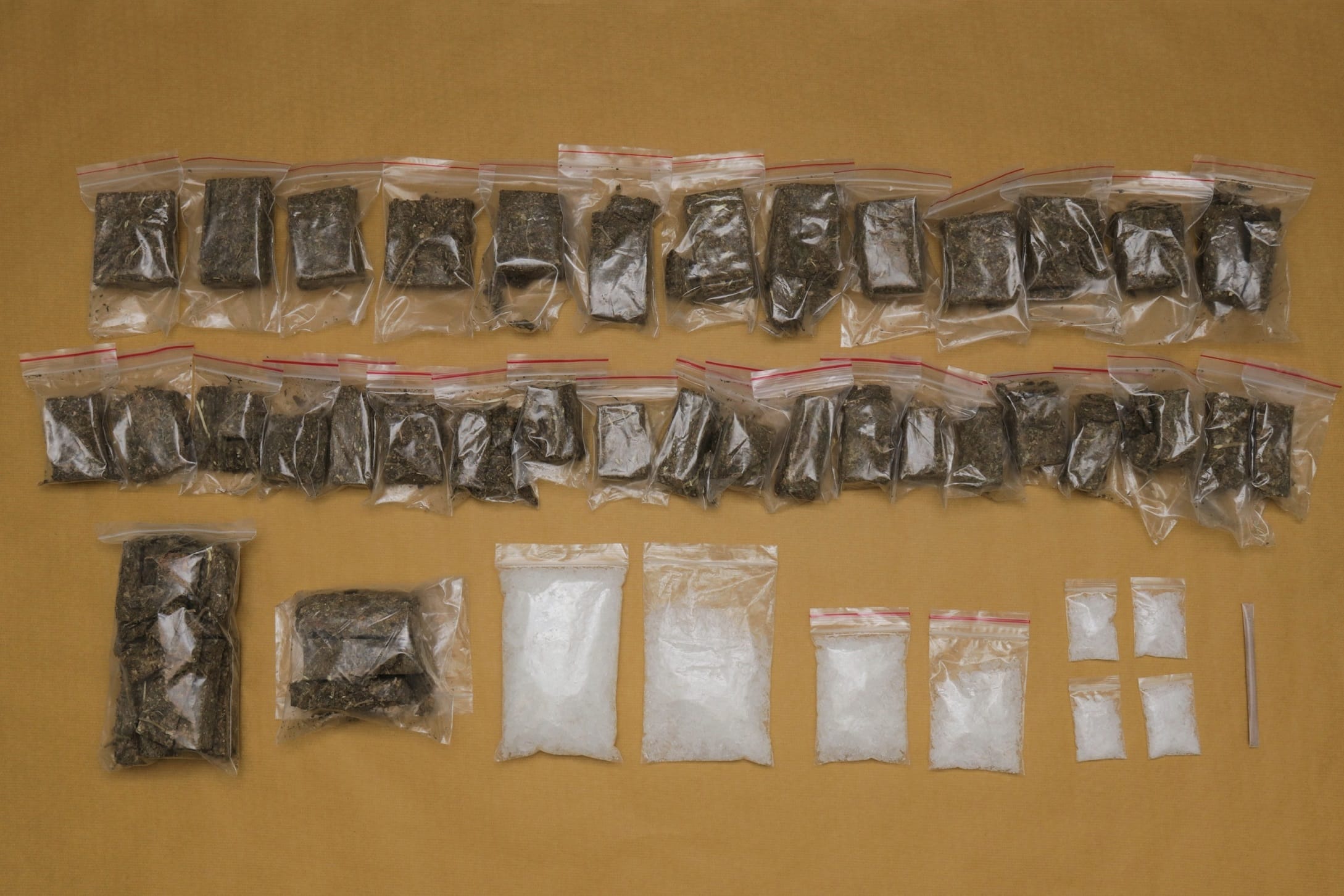 Plastic bags containing marijuana and crystal-like substances arranged on tan surface.