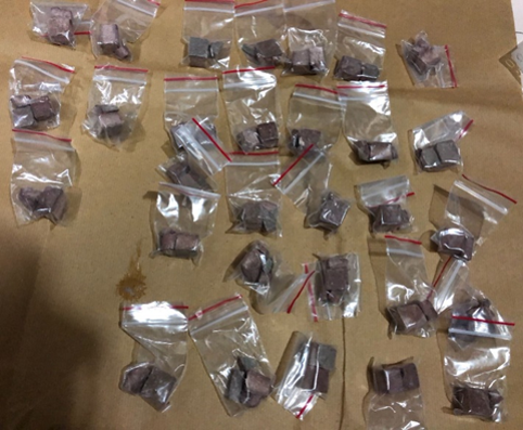 Multiple clear plastic bags, each containing dark brown, square-shaped contents, on brown surface.