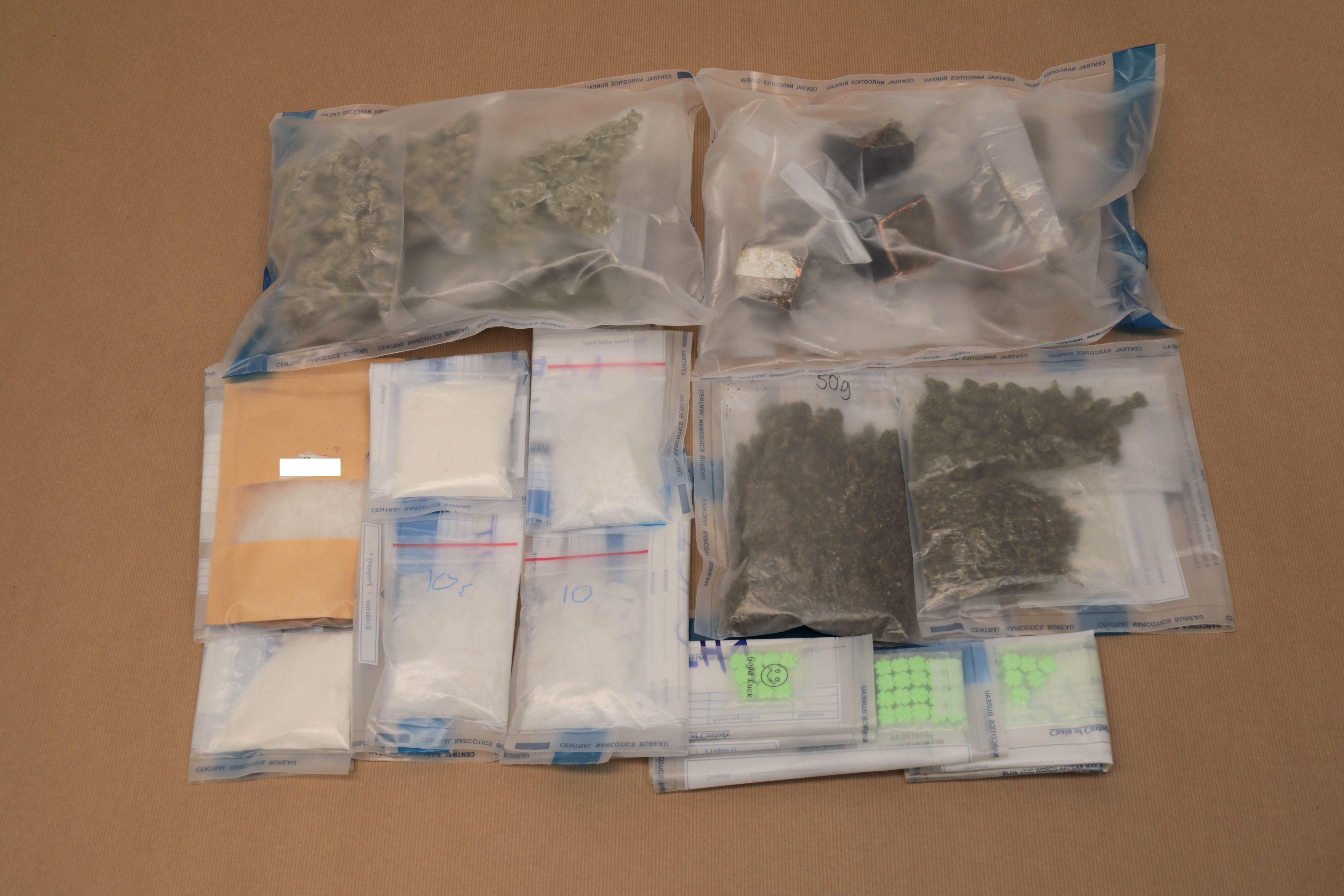 Evidence bags with marijuana, white powder, and green pills on a brown surface.