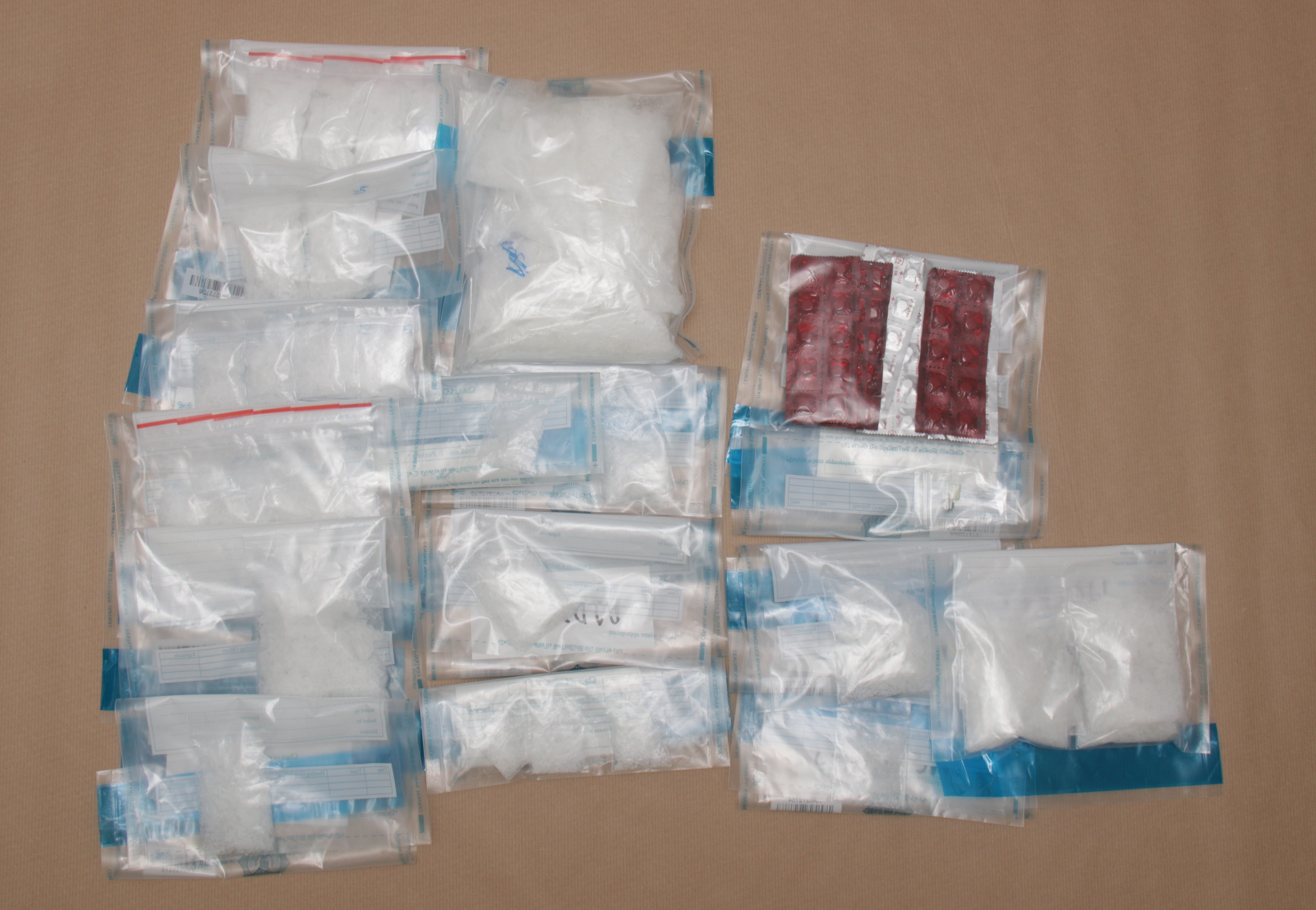 Sealed plastic bags with white powder and red pills are spread on a beige surface.