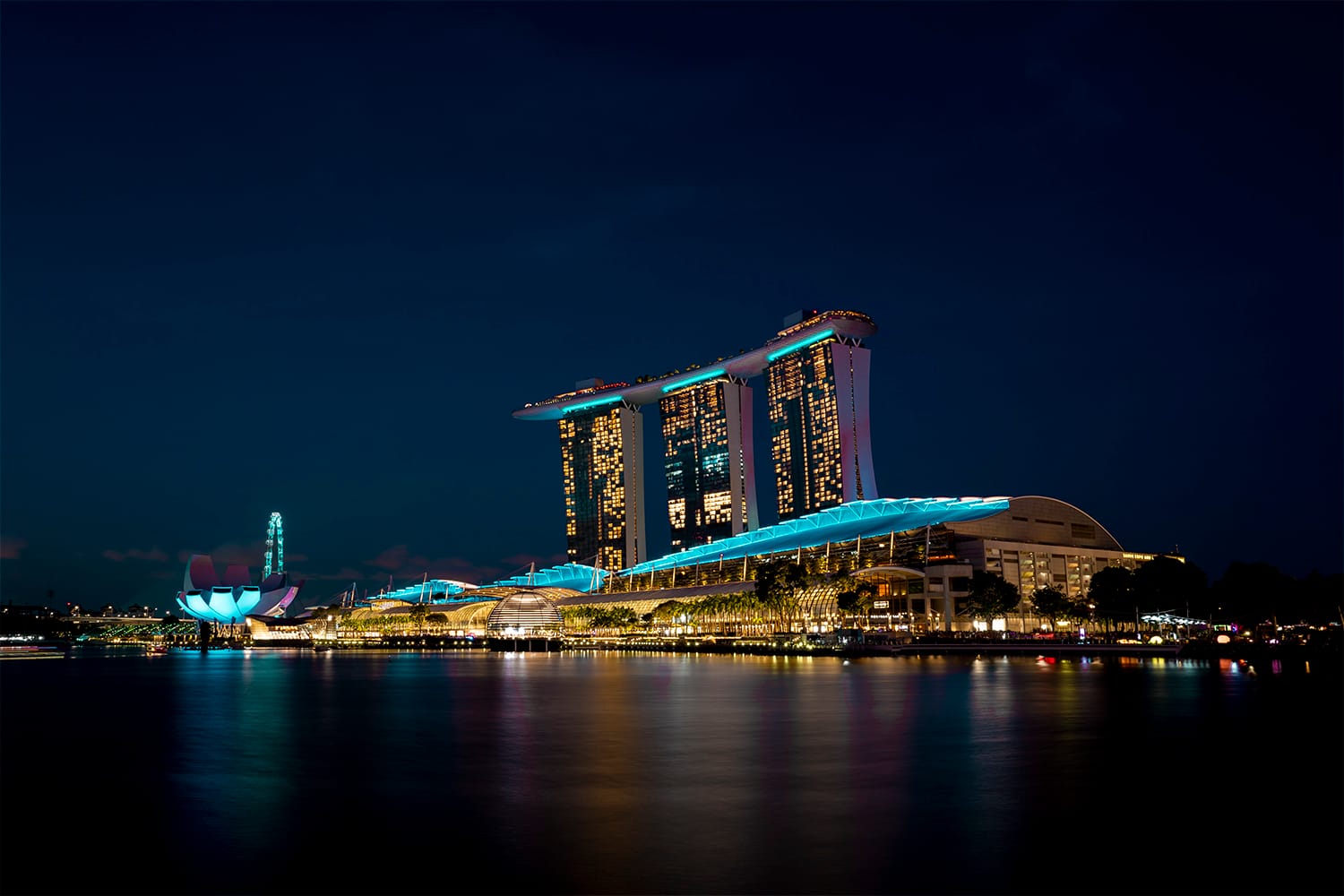 Night view of lit Marina Bay Sands with light reflections in the water.