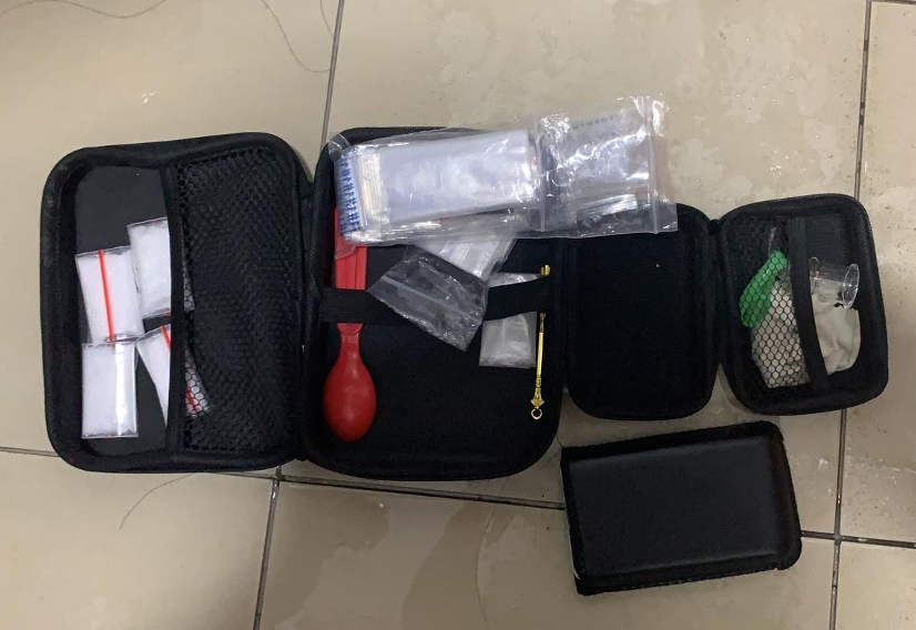 Open black kit showing tools, plastic bags and vials on a tiled surface.
