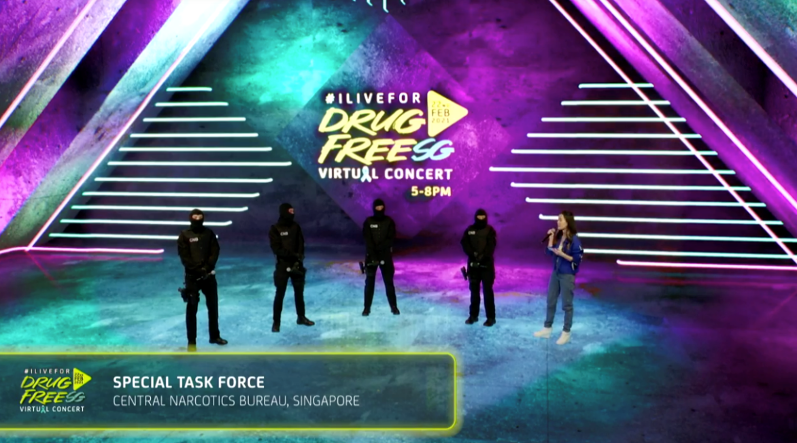 "Drug Free SG Virtual Concert" backdrop with 4 police and a speaker on stage.