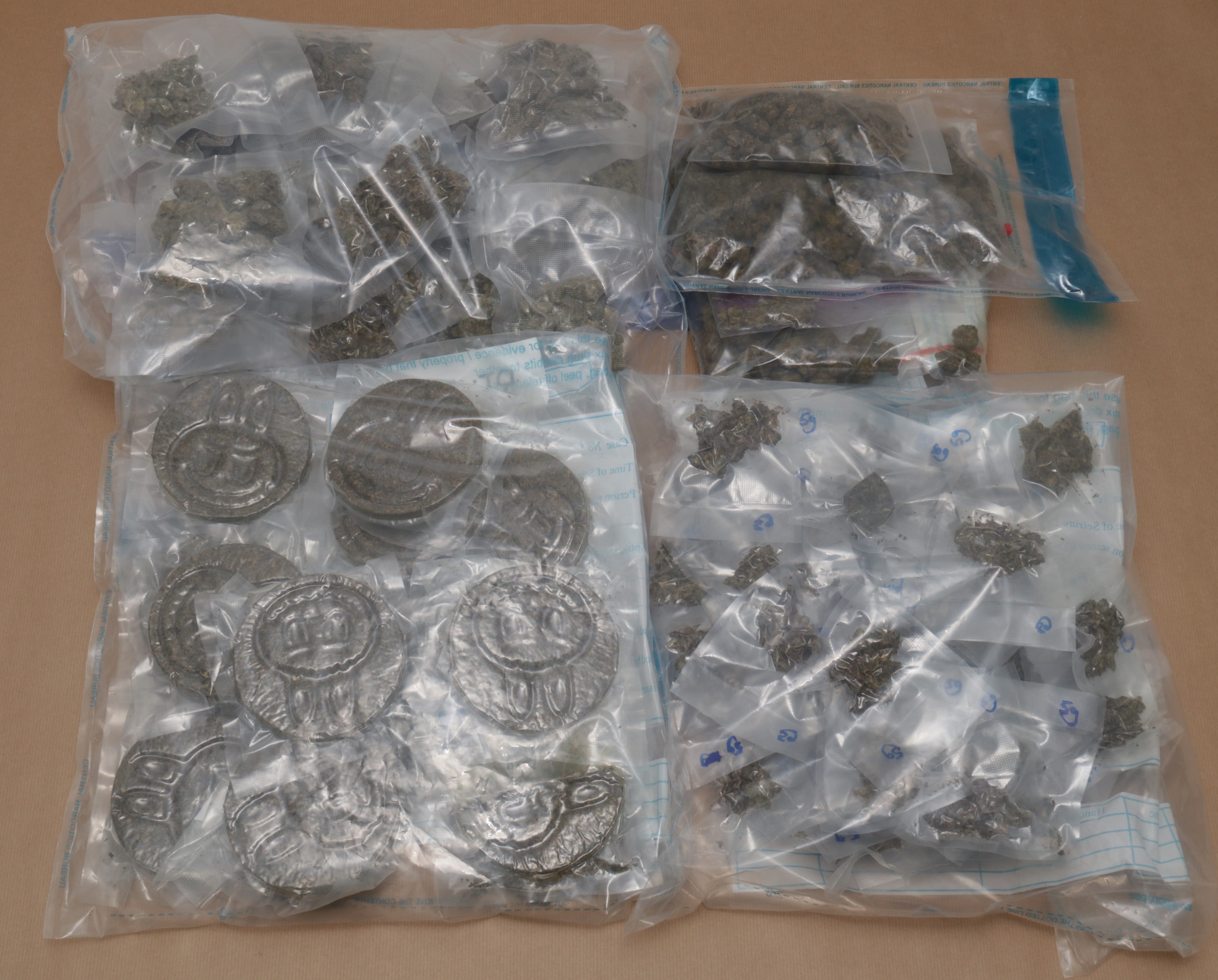 Sealed plastic bags contain cannabis and round slabs with stamped designs on a brown surface.